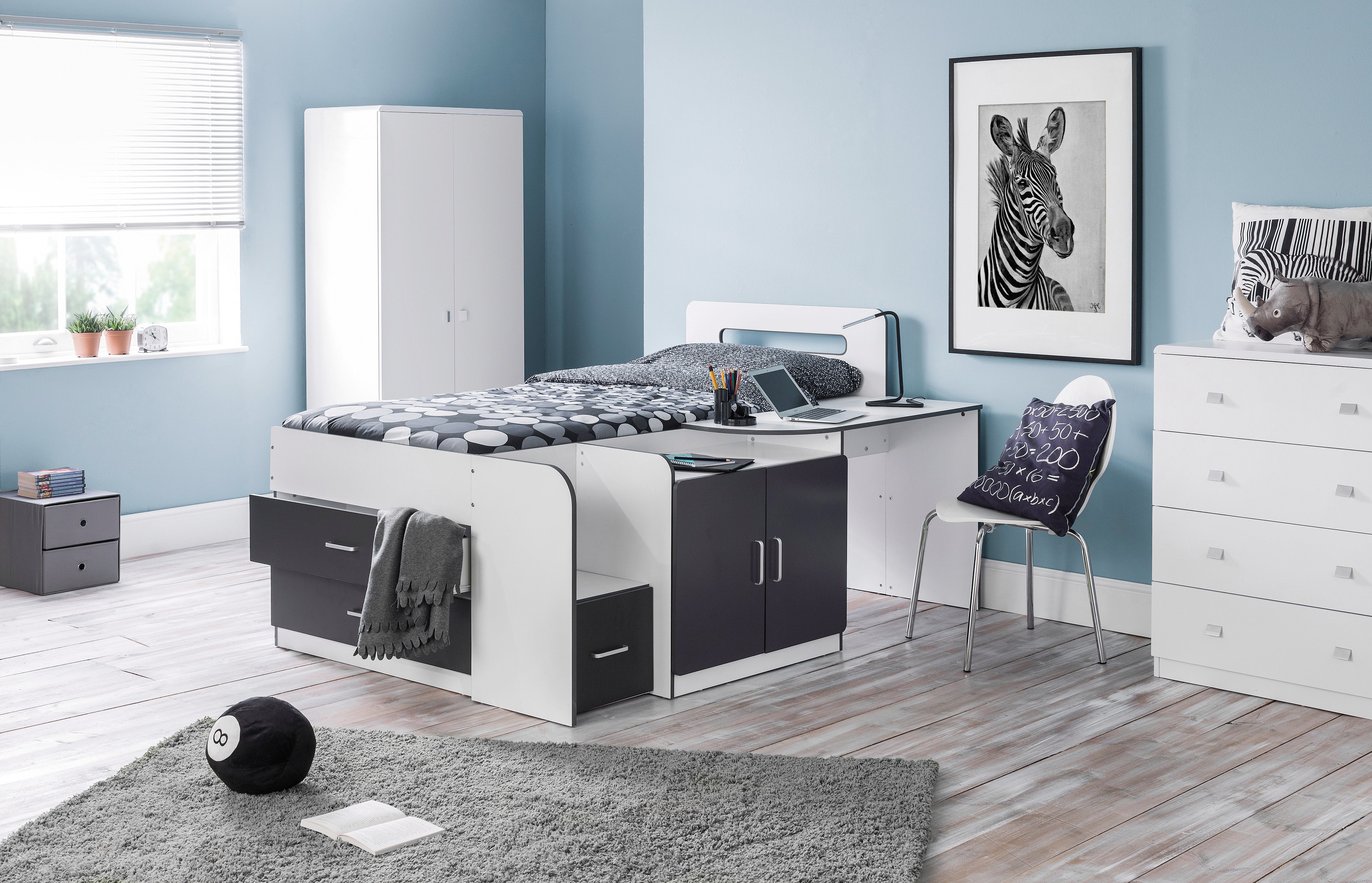 Modern bedroom with white bed, desk, and wardrobe against a light blue wall.