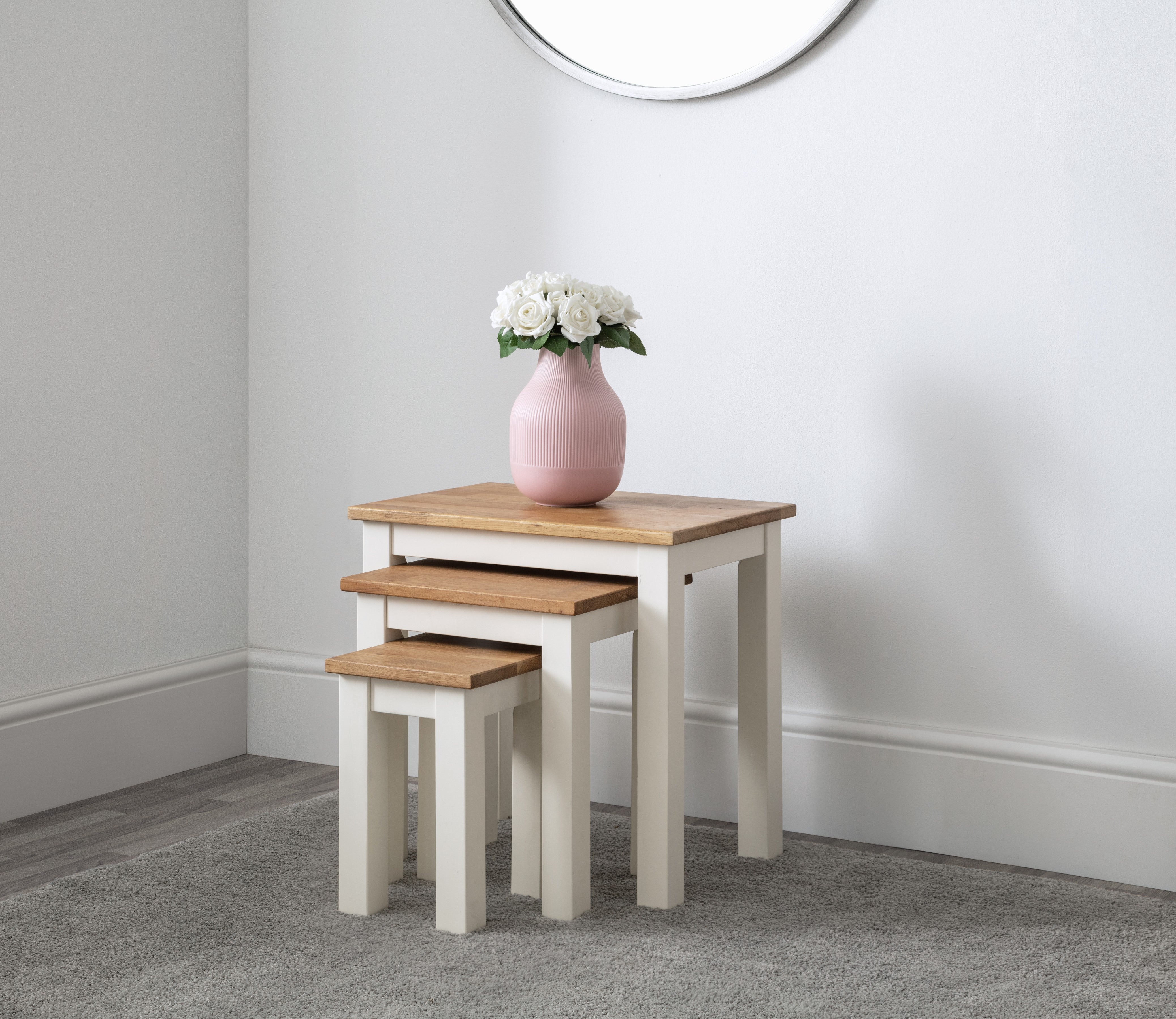 Set of three nesting tables with a pink vase and flowers on a plain wall background