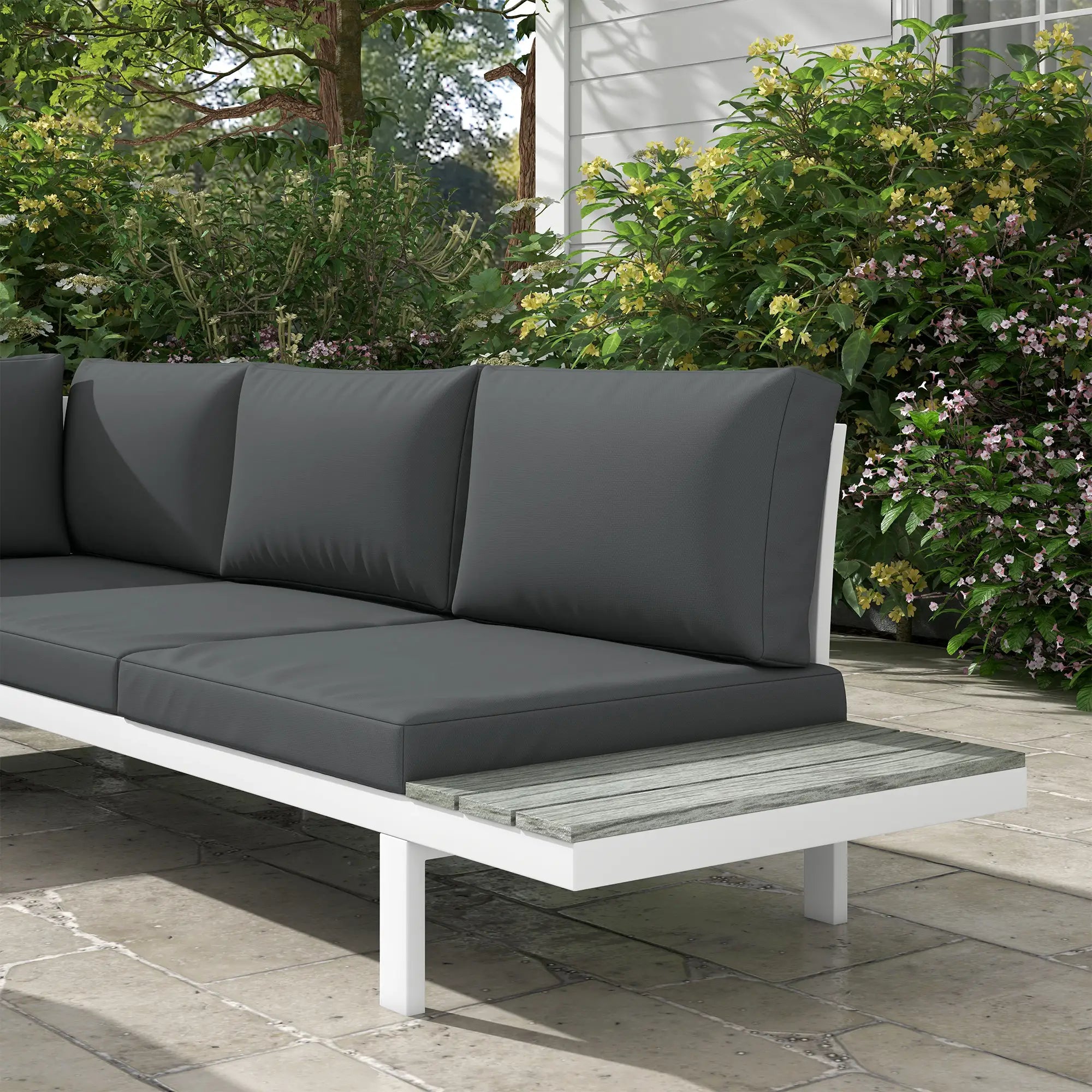 Gray outdoor sofa with cushions on a stone patio, surrounded by greenery.