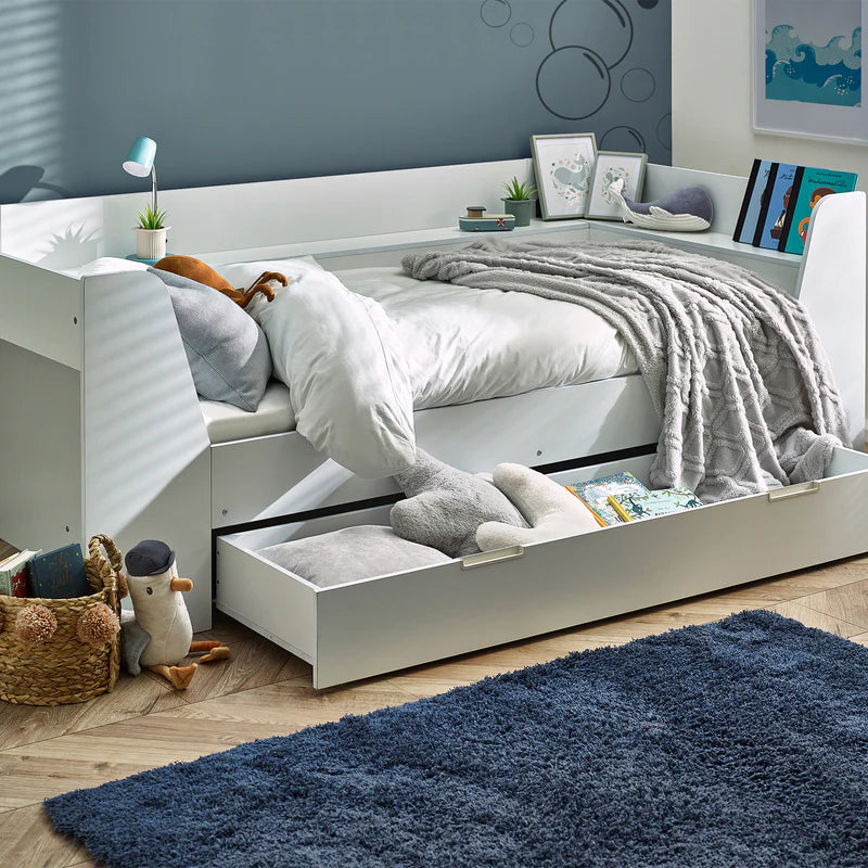 White bed with storage drawers in a room with a blue rug and wall art.
