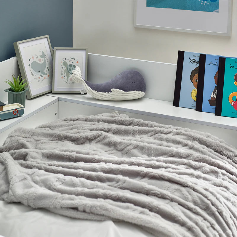 Gray textured blanket on a bed with decorative pillows and books in the background.