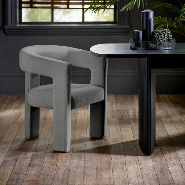 Gray chair next to a black dining table with decorative items on a wooden floor.