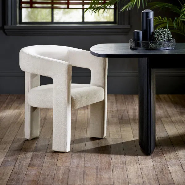 Beige chair next to a black table in a room with wooden flooring and a window in the background.