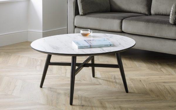 Round marble coffee table with a cup and book on a wooden floor in a living room setting.