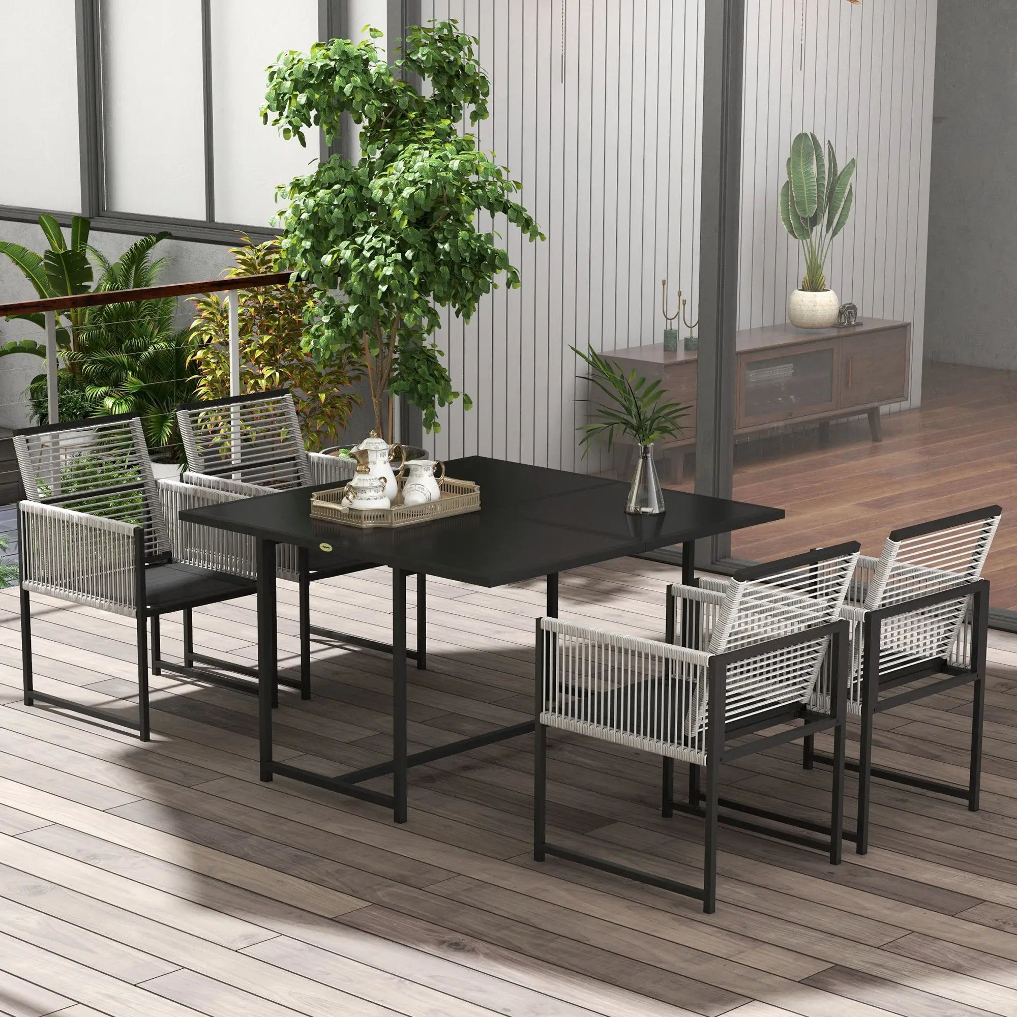 Outdoor dining set with black table and chairs on a wooden deck, surrounded by plants.