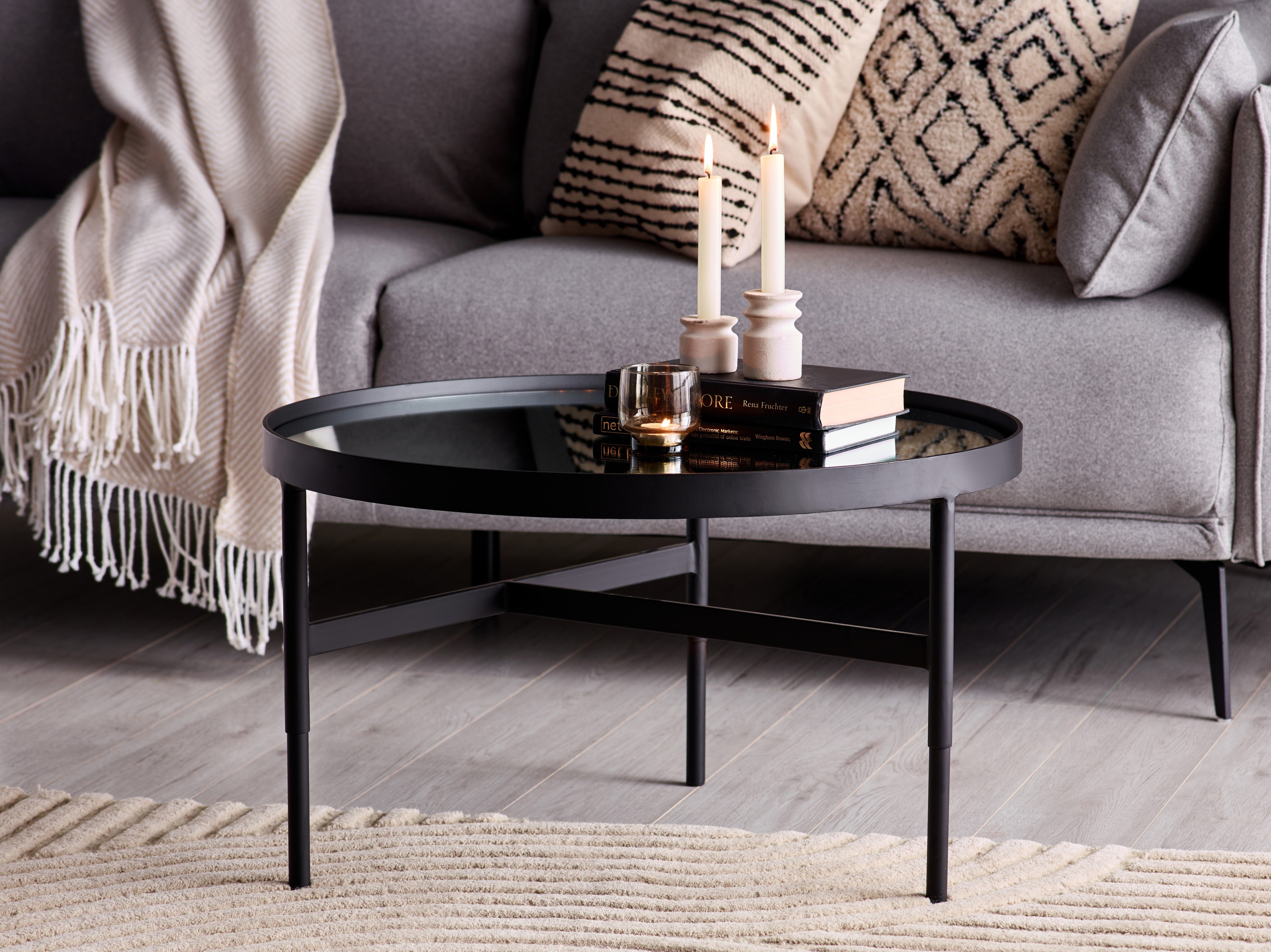 Round black coffee table in front of a gray sofa with decorative items on it.