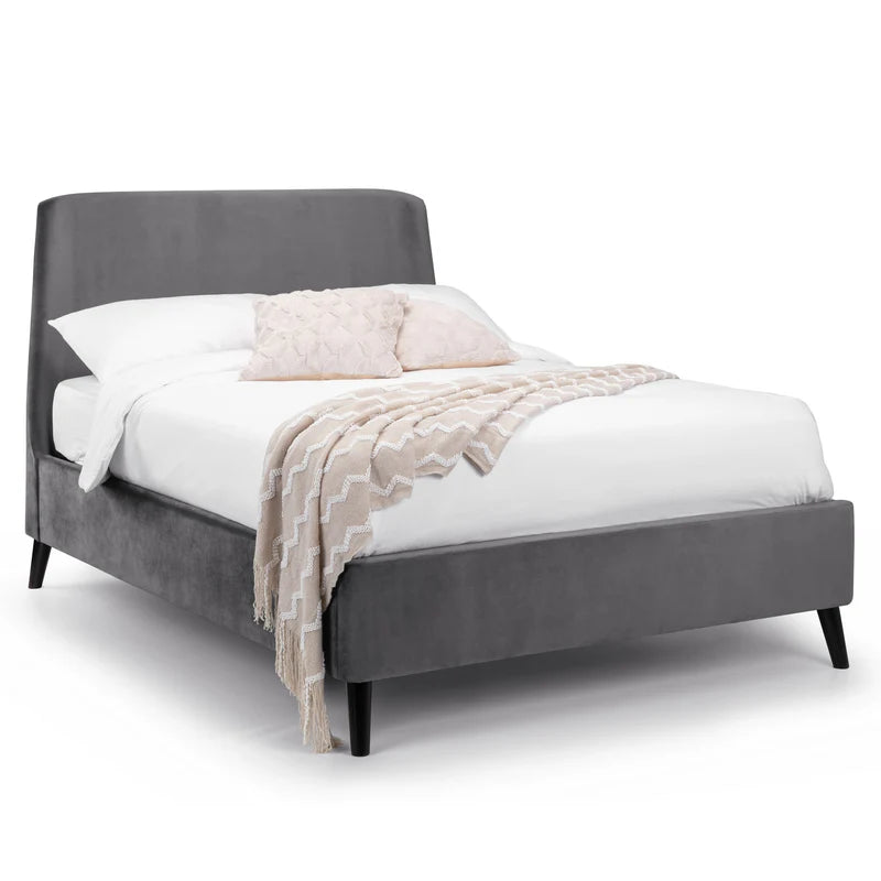 Gray upholstered bed with white bedding and a beige blanket on a white background