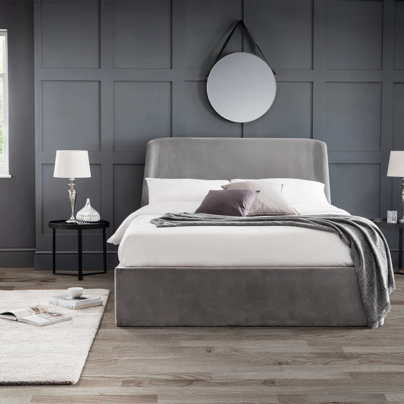 Gray upholstered bed in a modern bedroom with gray walls and wooden flooring.