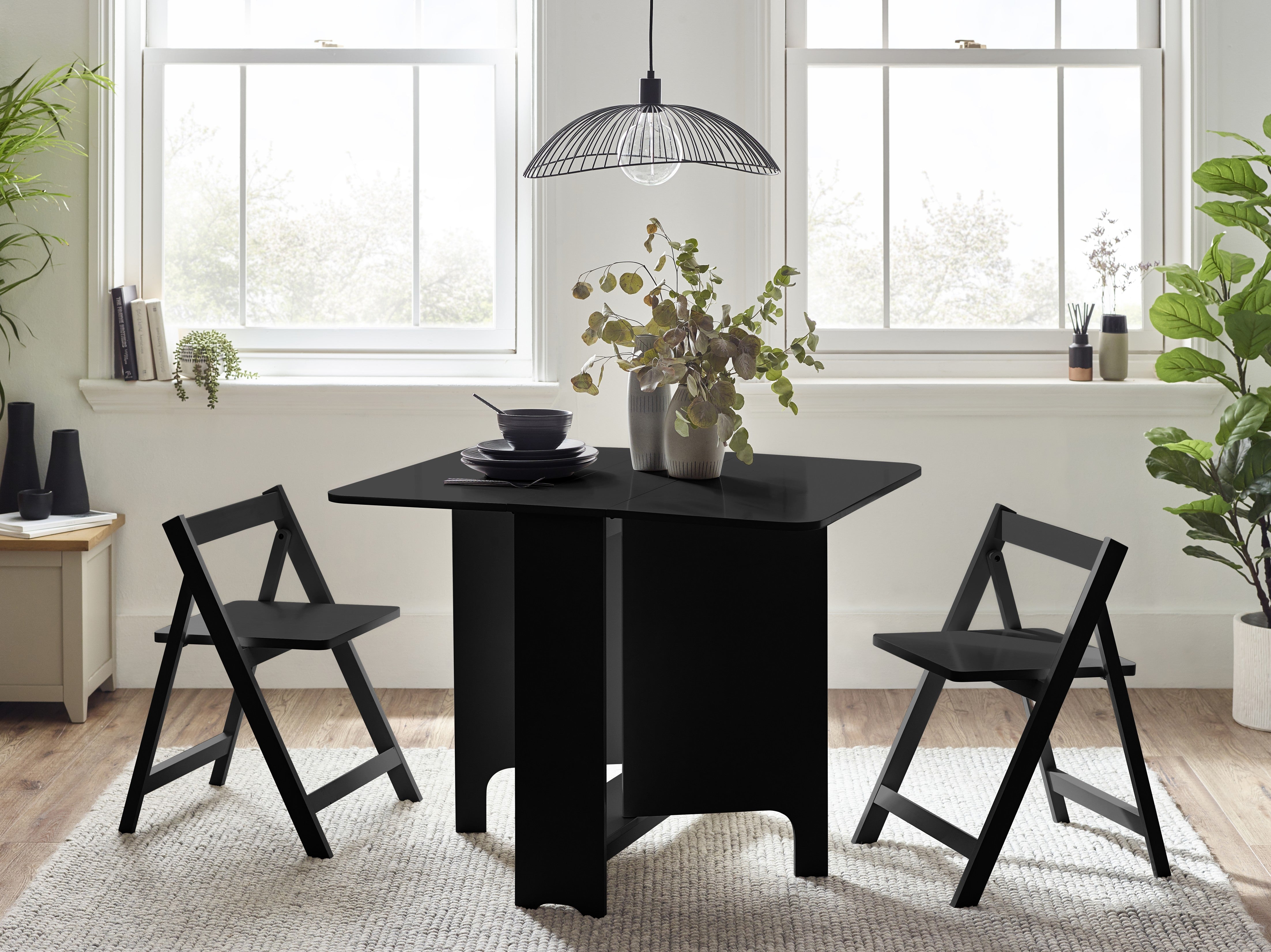 Black dining table with two chairs in a bright room with large windows.