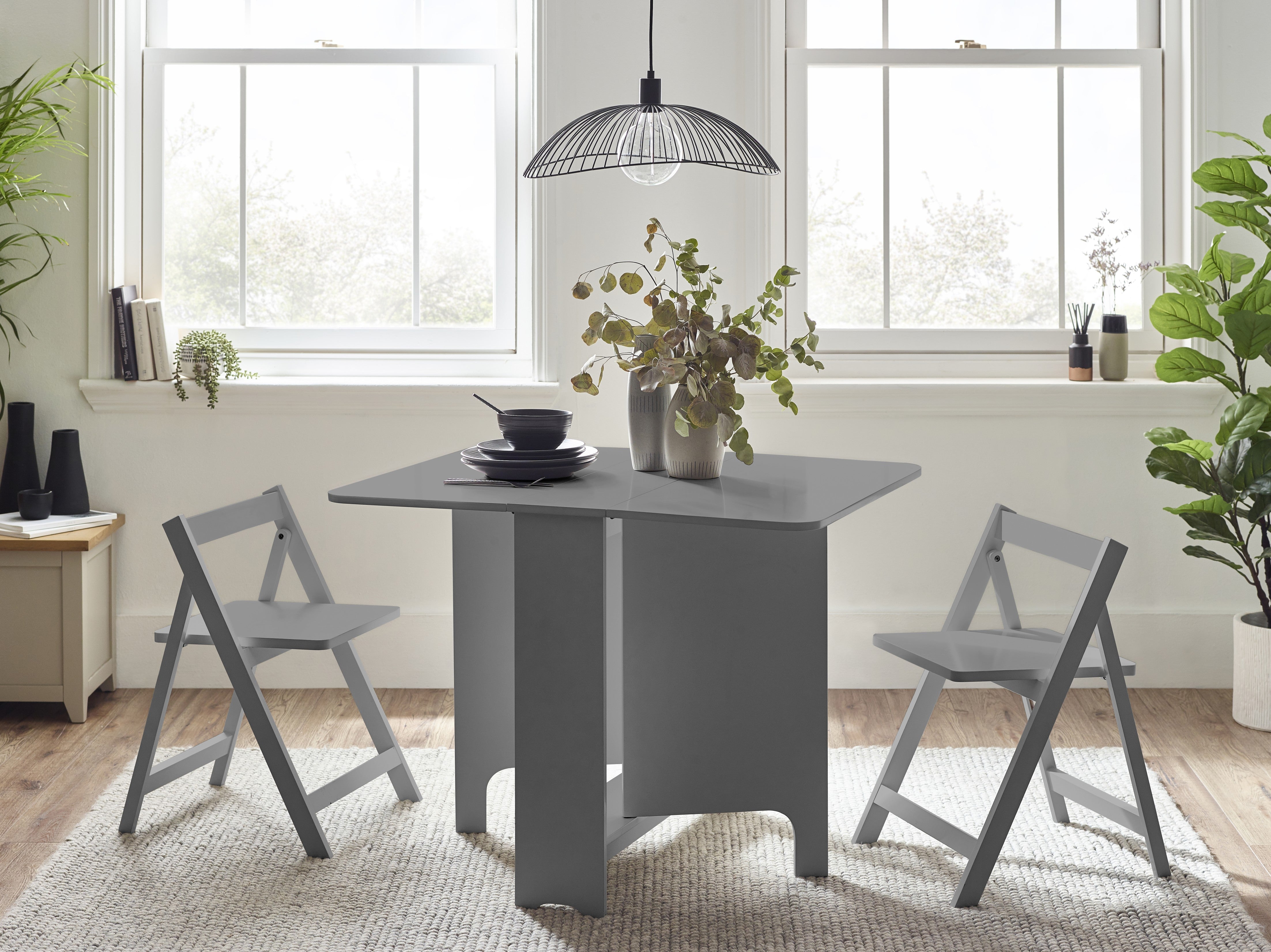 Gray dining table with two chairs in a bright room with large windows.