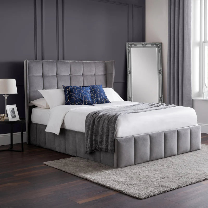 Gray upholstered bed in a bedroom with a mirror and lamp.