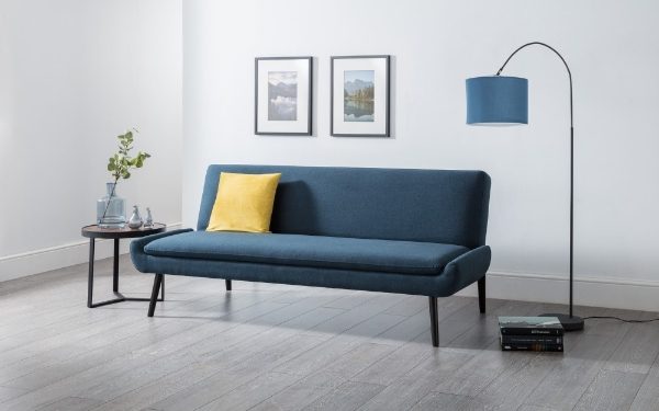 Blue sofa with a yellow pillow in a room with a lamp and small table.