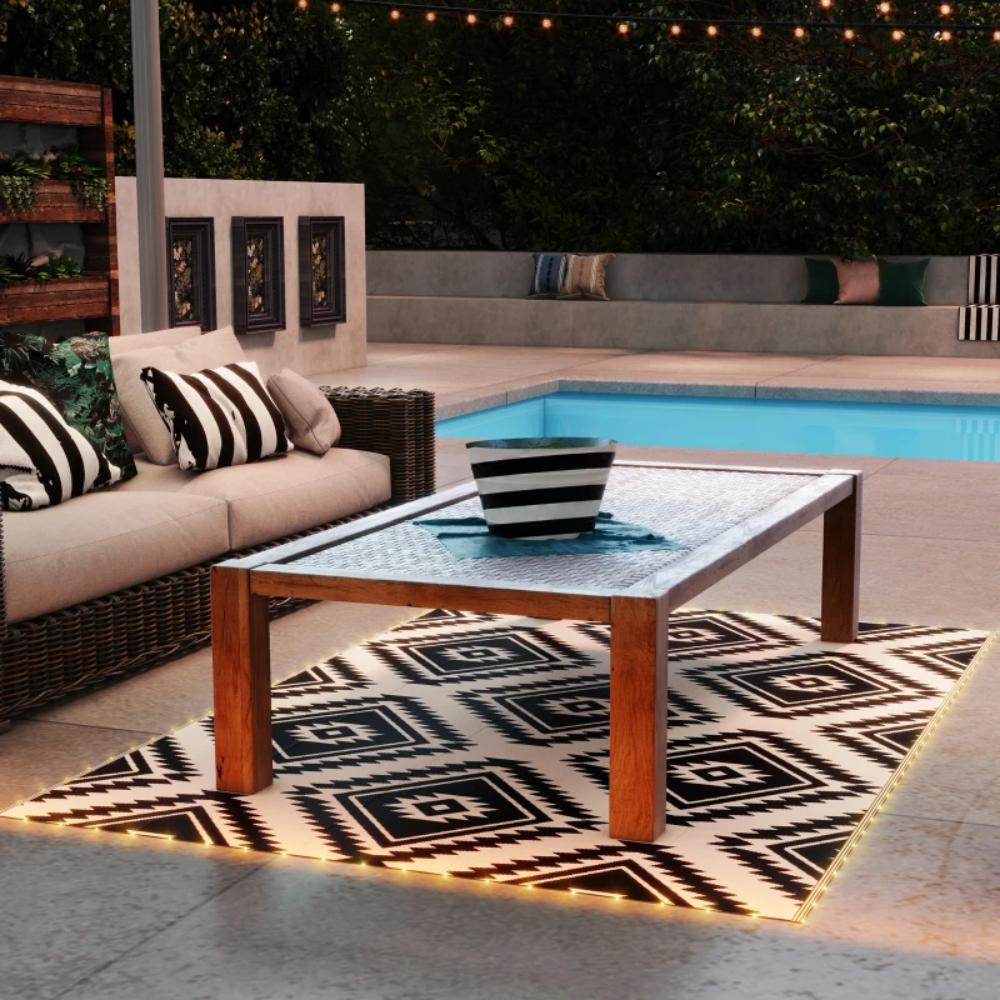 Outdoor patio with a coffee table, sofa, and rug near a pool at night.