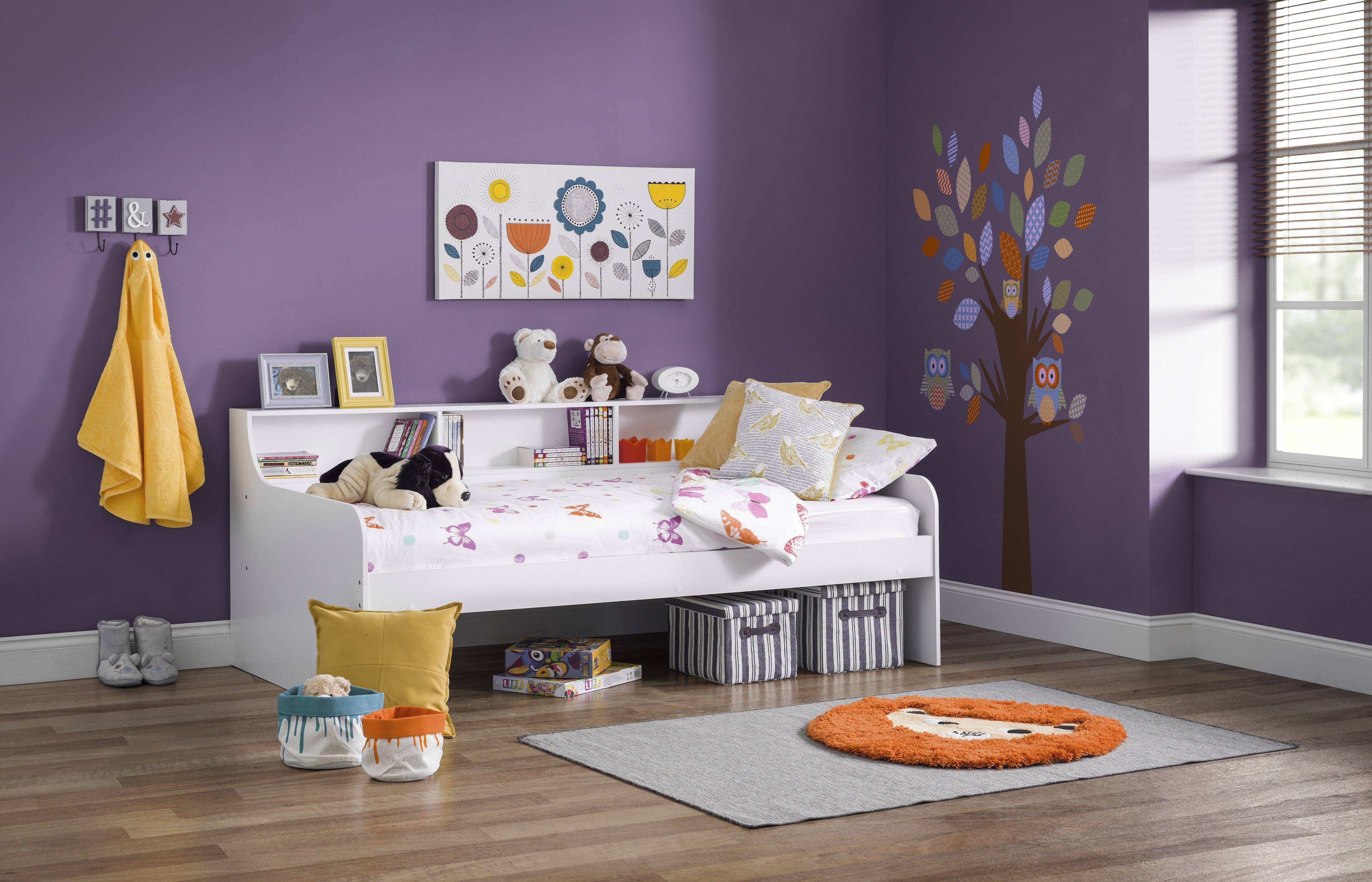 Children's bedroom with purple walls, a bed, toys, and decorative items.