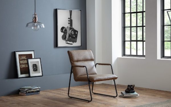 Brown leather chair in a room with framed pictures on the wall and large windows.