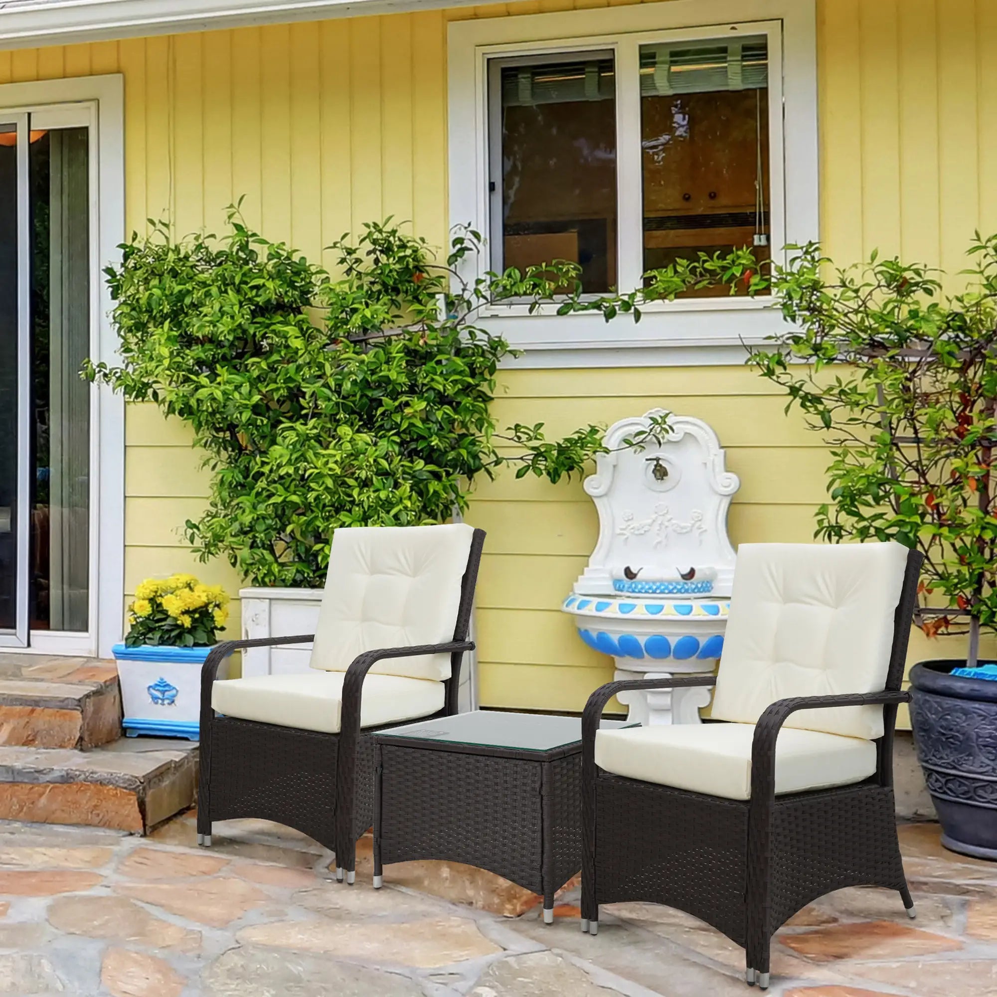 Outdoor patio set with two chairs and a small table on a stone patio in front of a yellow house.