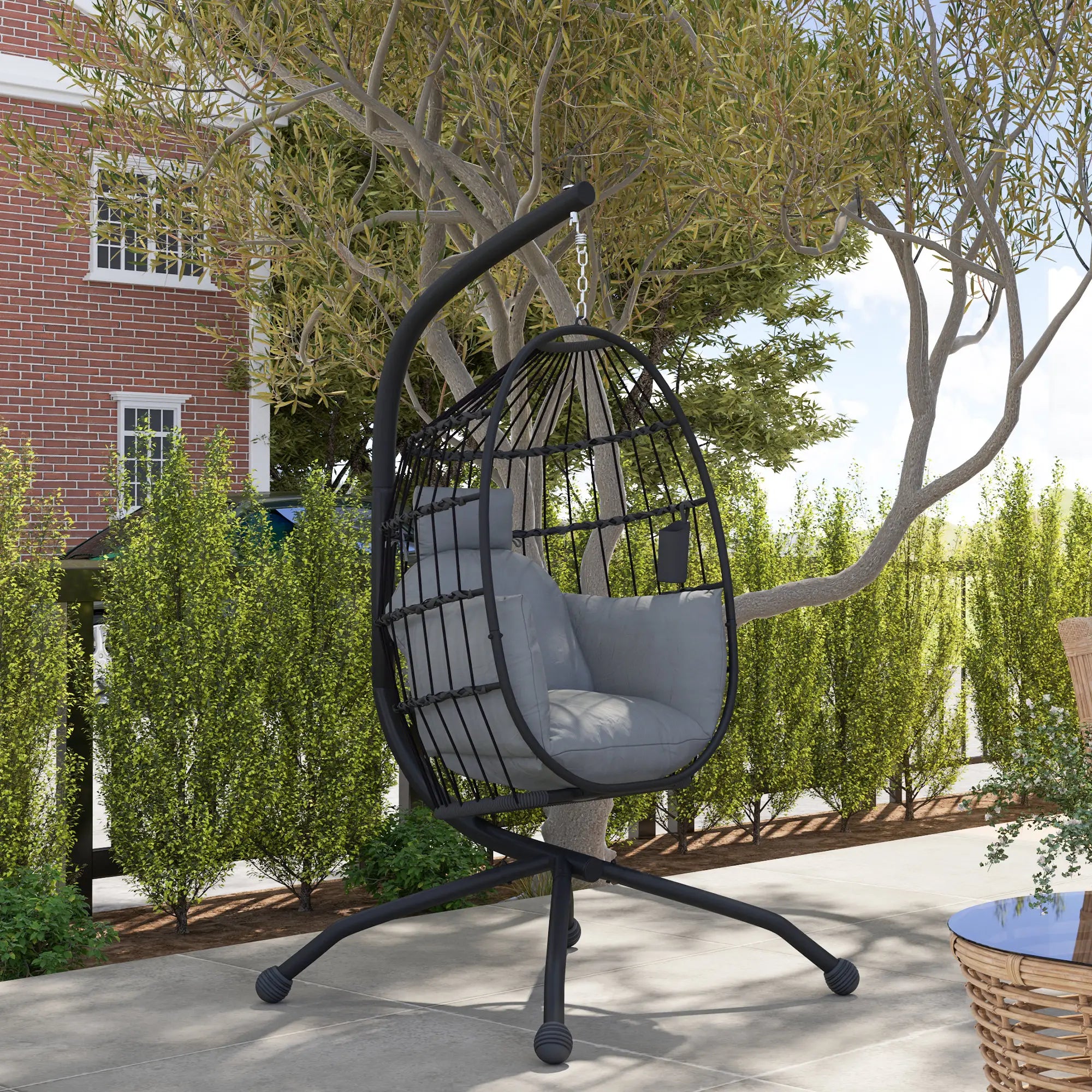 Black hanging chair with gray cushion on a patio with trees and building in the background