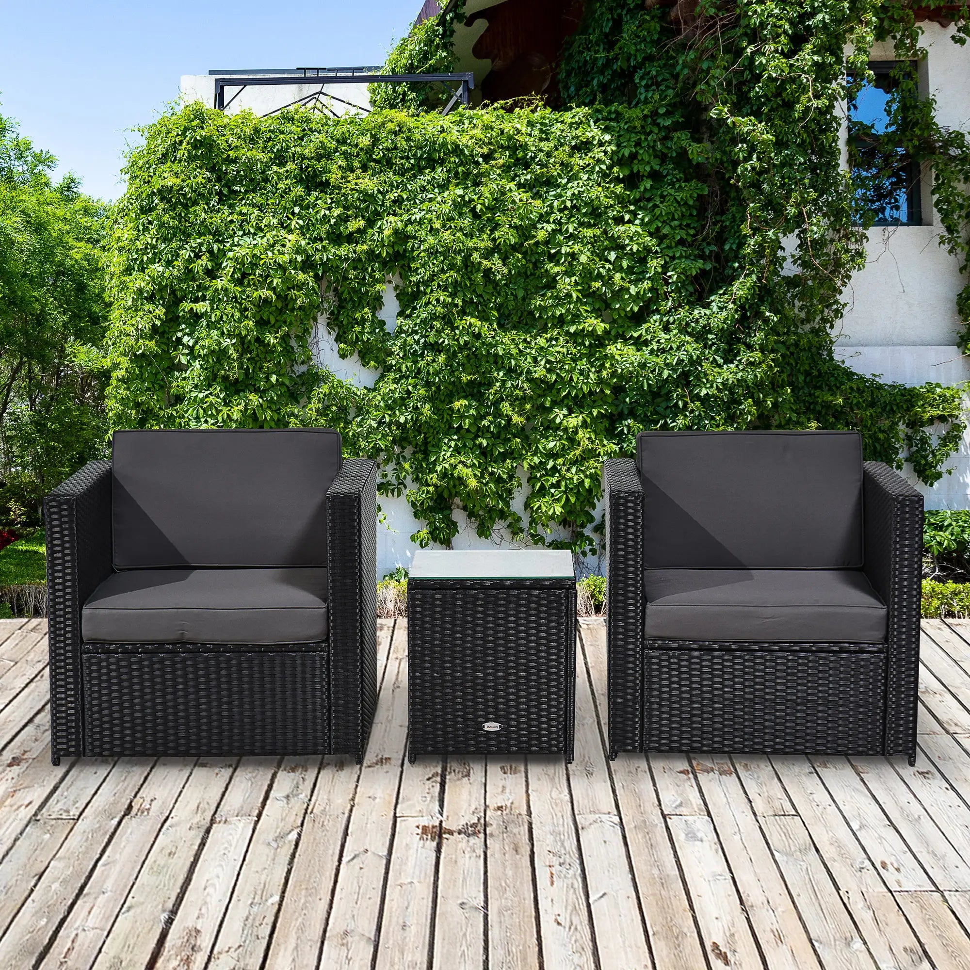 Outdoor furniture set with two dark wicker chairs and a small table on a wooden deck, surrounded by greenery.