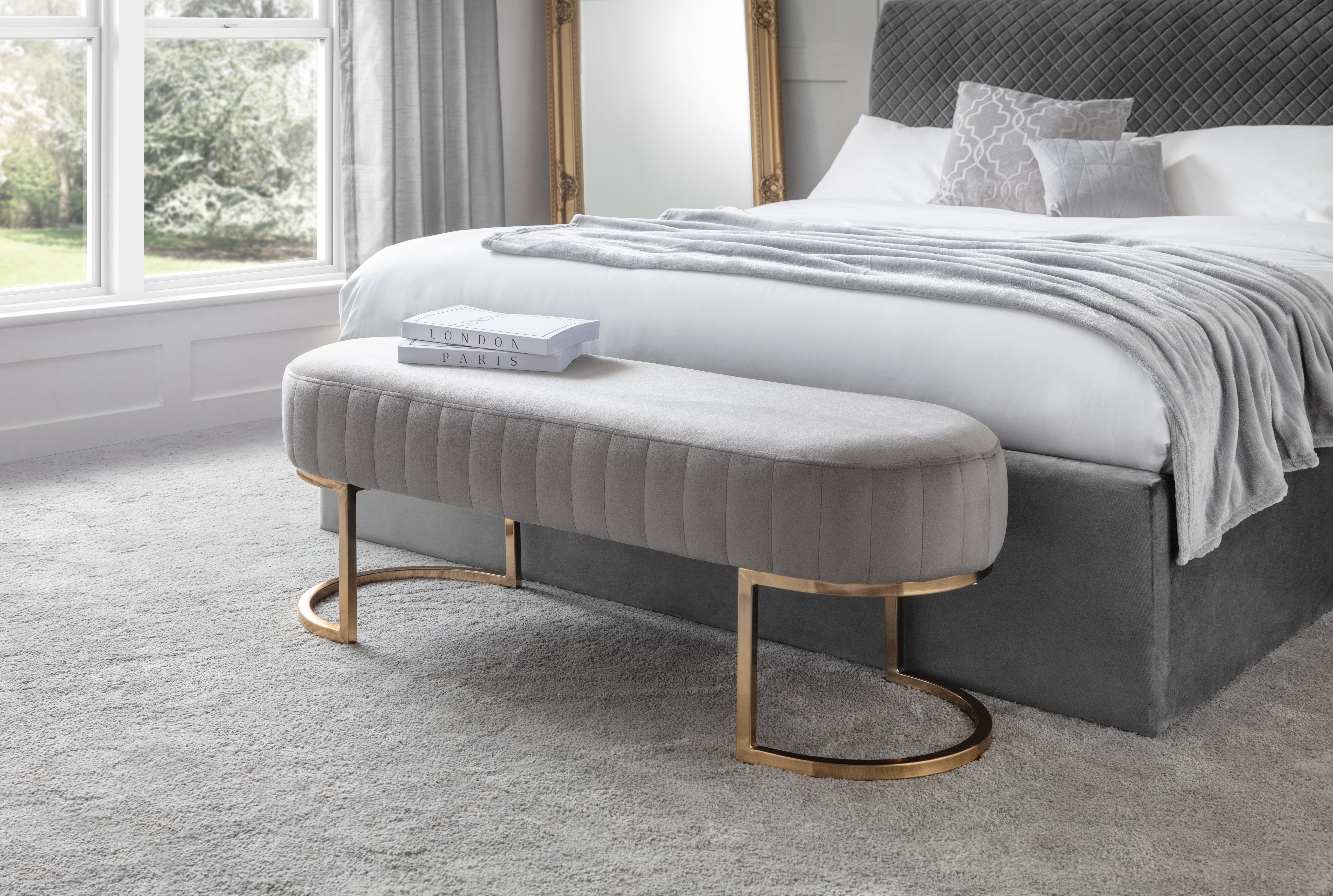 Gray upholstered bench in front of a bed with white bedding and gray headboard.