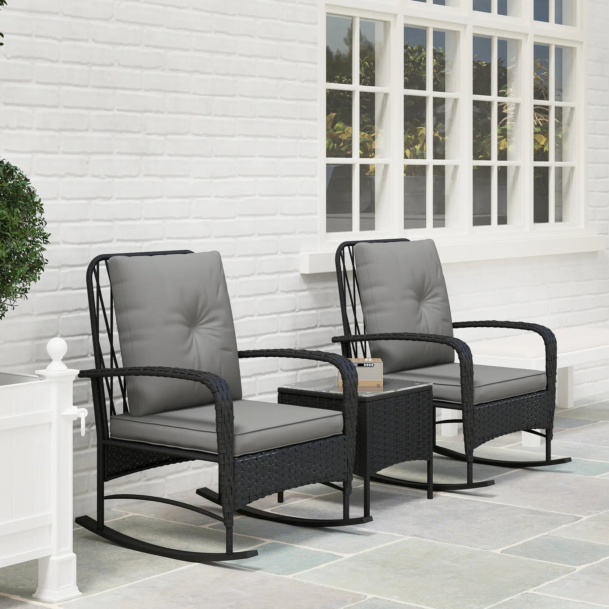 Two outdoor chairs with gray cushions on a patio with a white brick wall background.