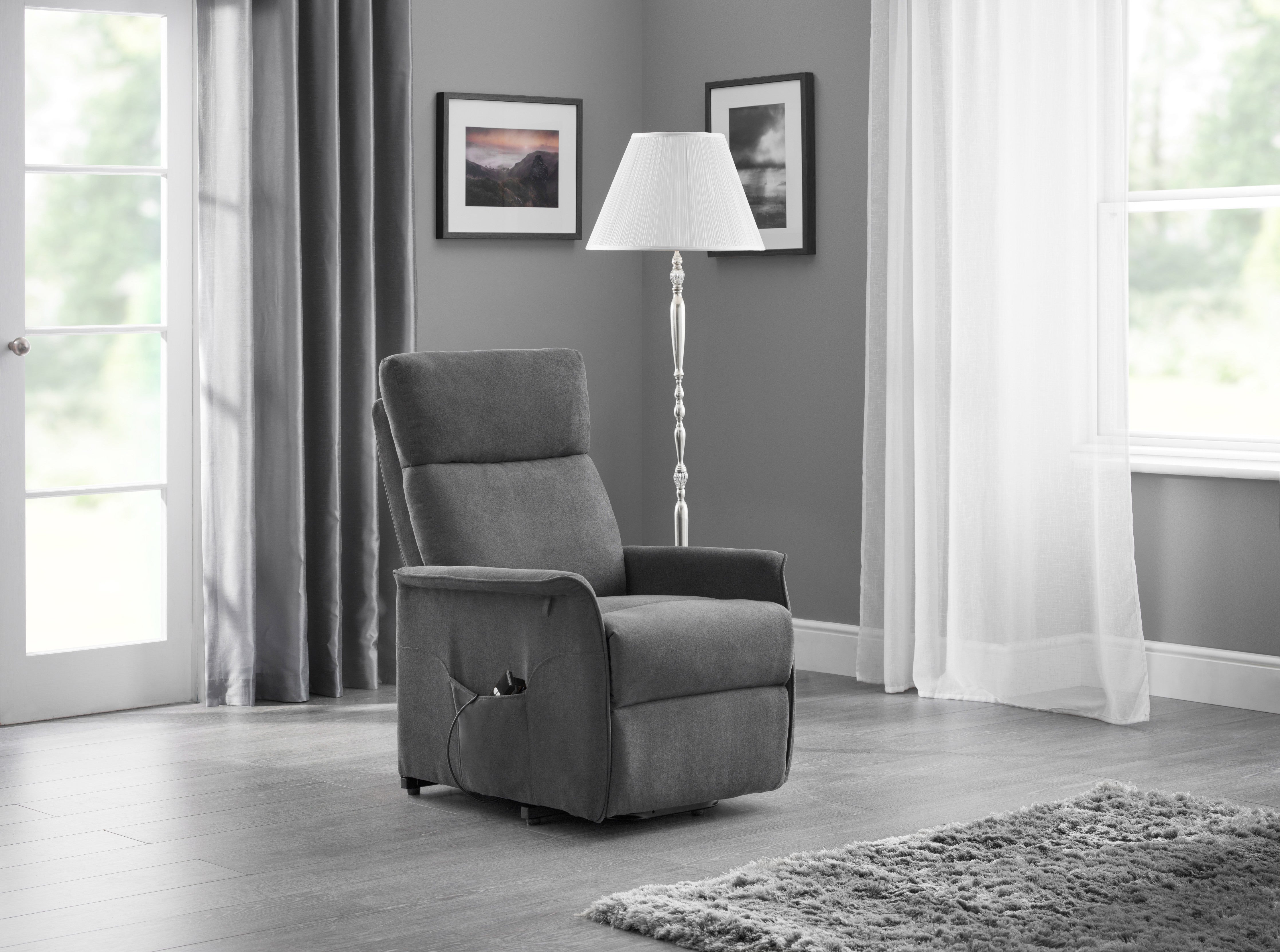 Gray recliner chair in a living room with a lamp and framed pictures on the wall.