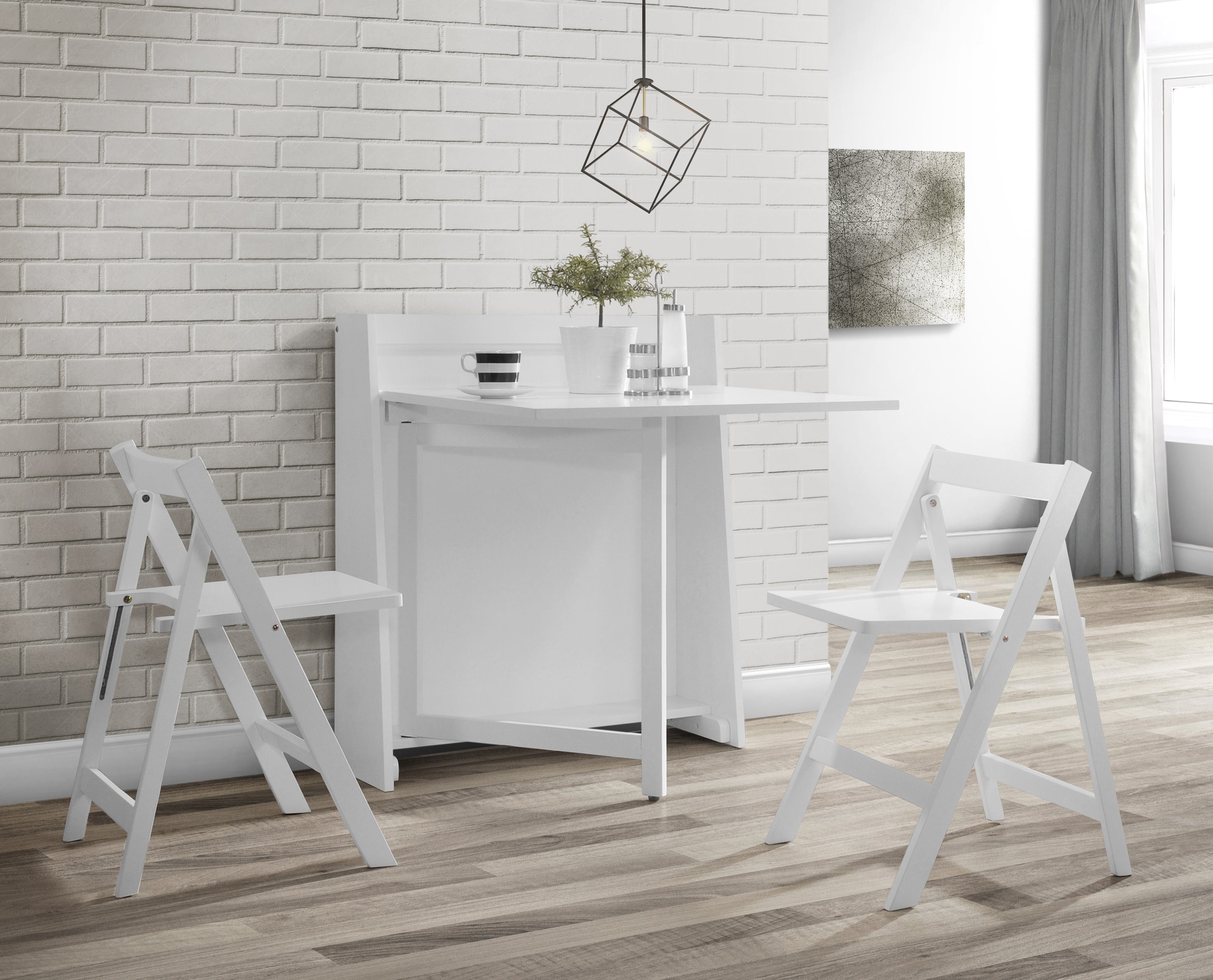 White folding table with two chairs in a room with a brick wall and window.