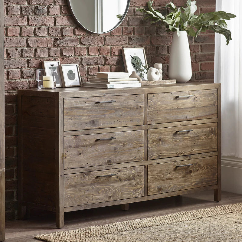 Wooden dresser with decorative items against a brick wall.
