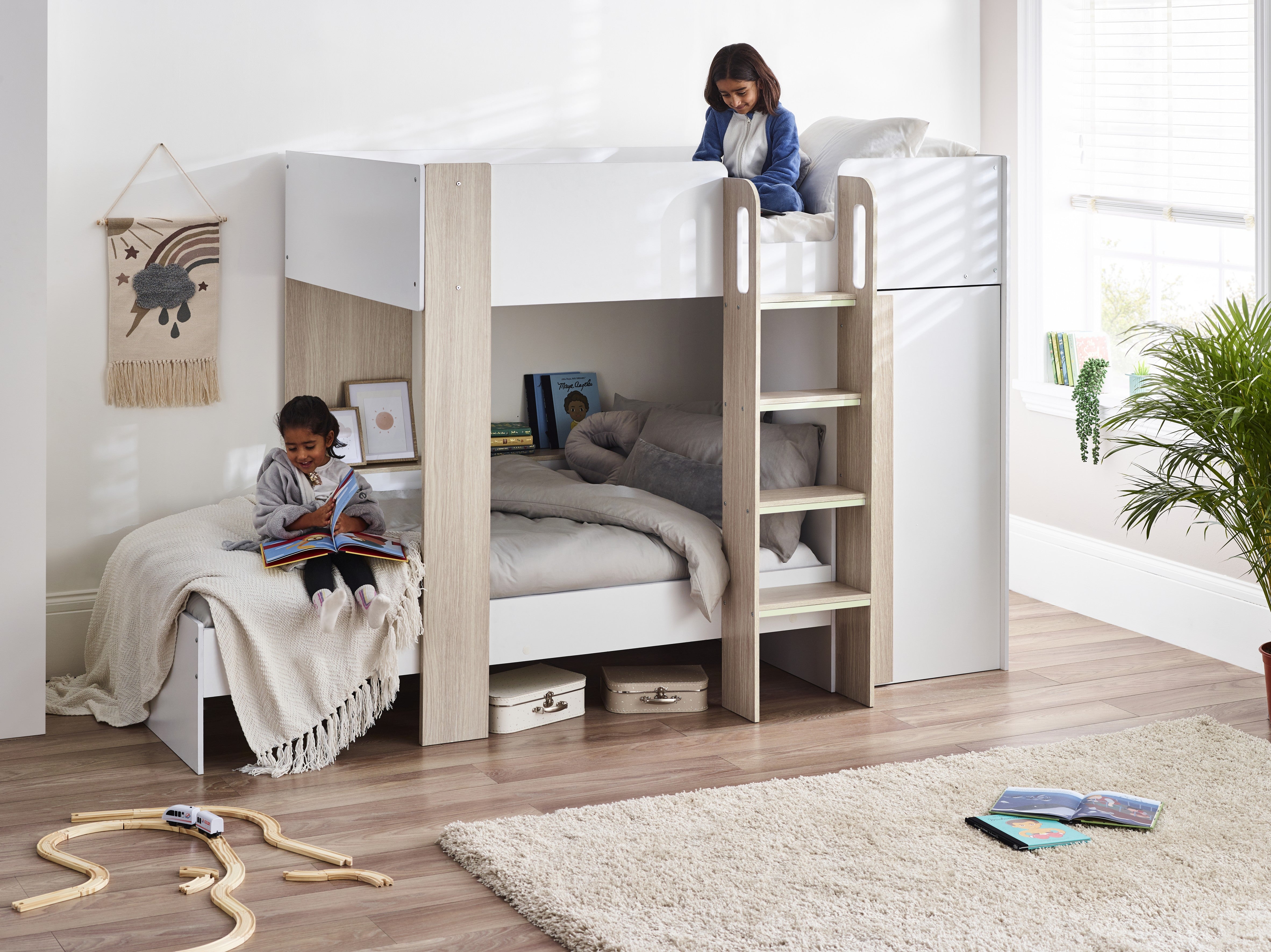 Children playing on a white bunk bed in a bright room with toys and books.
