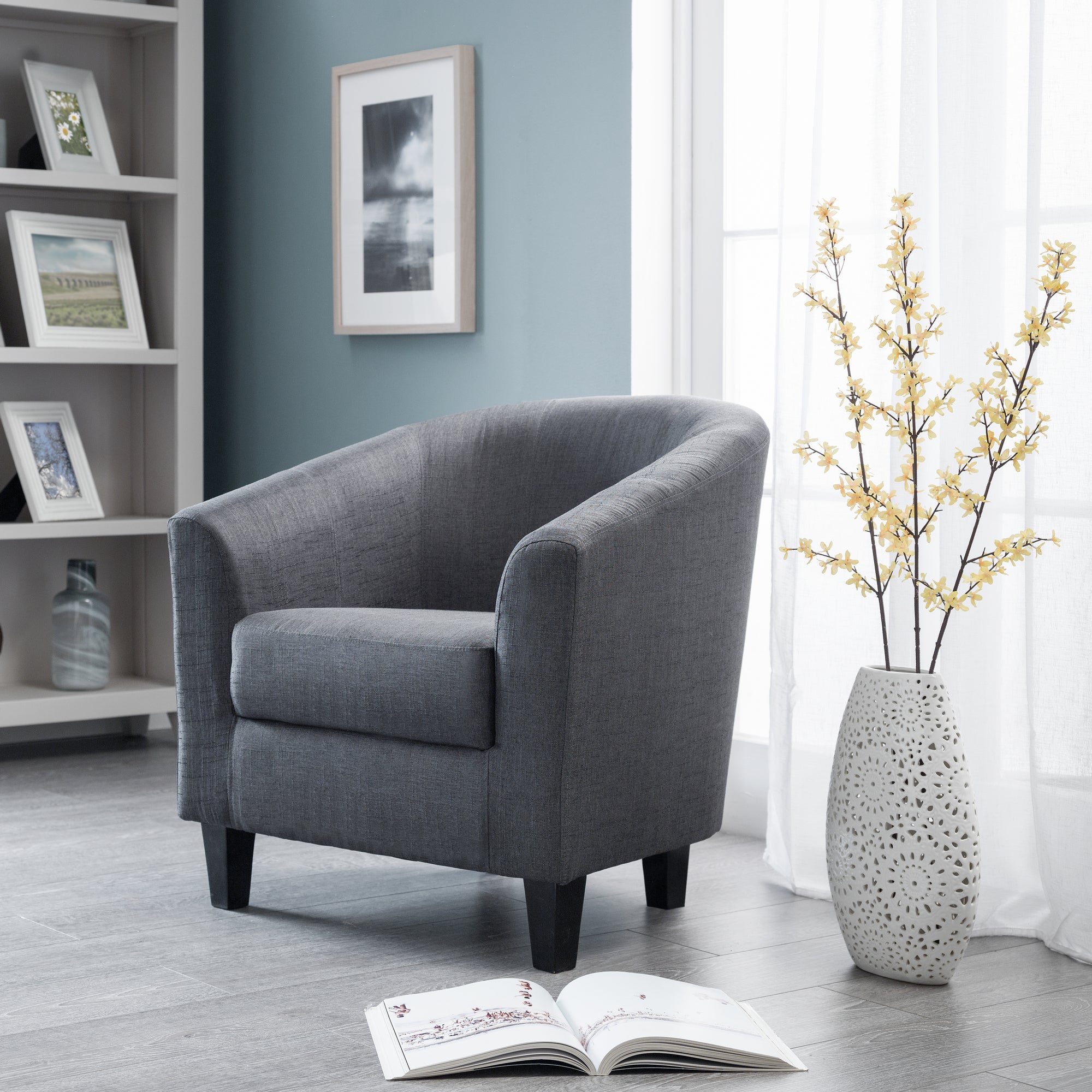 Gray armchair in a room with a book, vase, and framed pictures on a shelf.