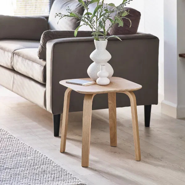 Wooden side table with a vase and plant in front of a gray sofa.