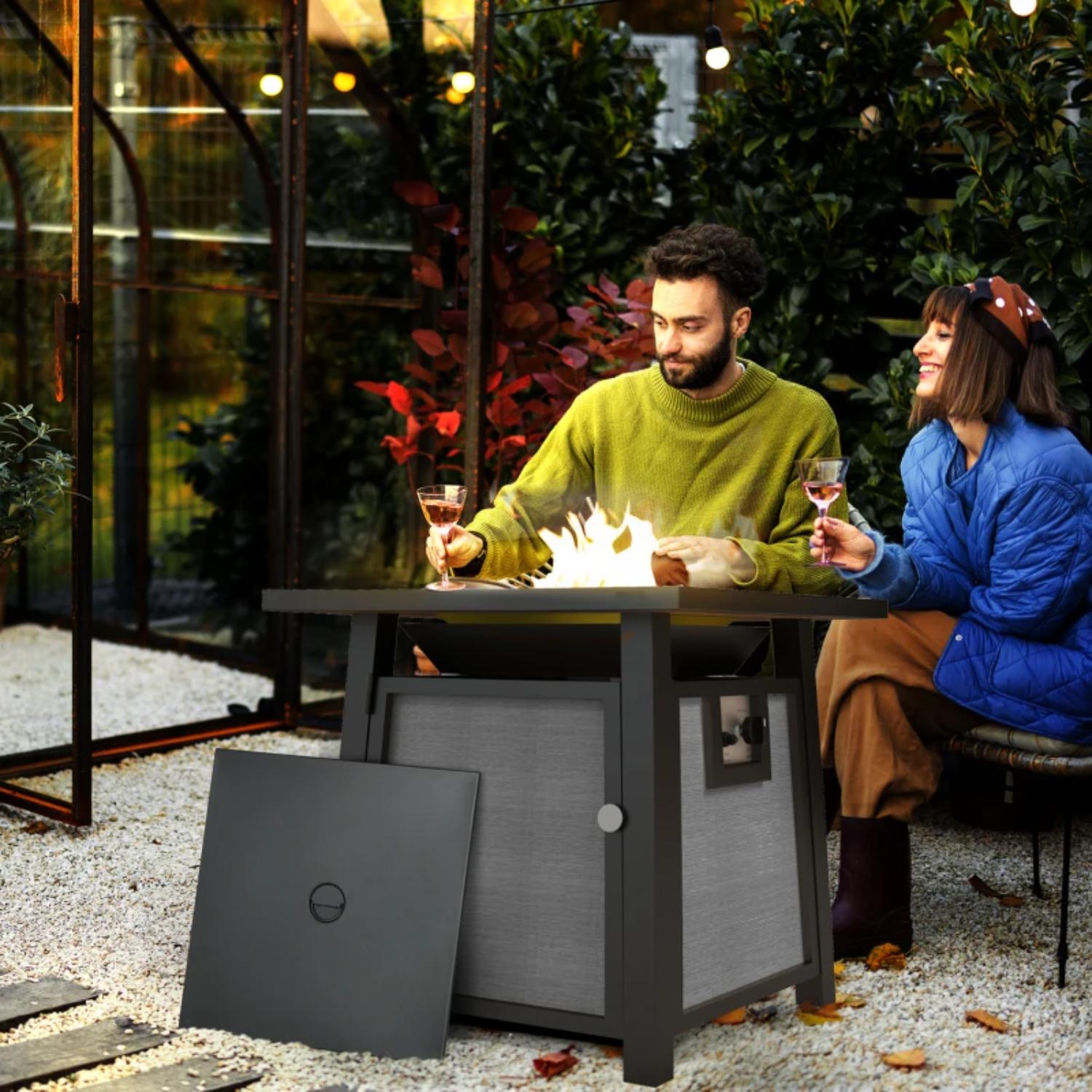 Two people sitting at a fire pit table in an outdoor setting, enjoying wine.