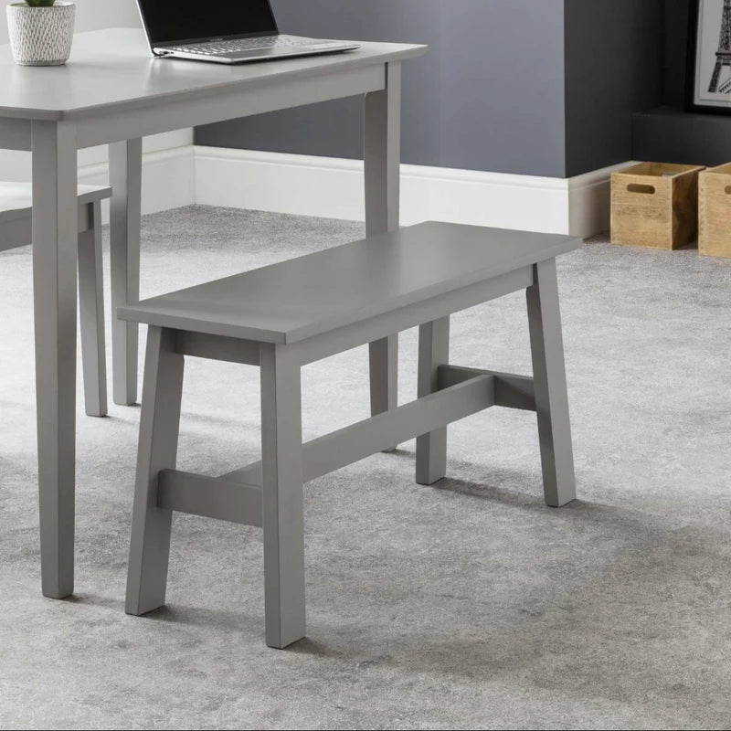 Gray bench in front of a gray table with a laptop on a carpeted floor.
