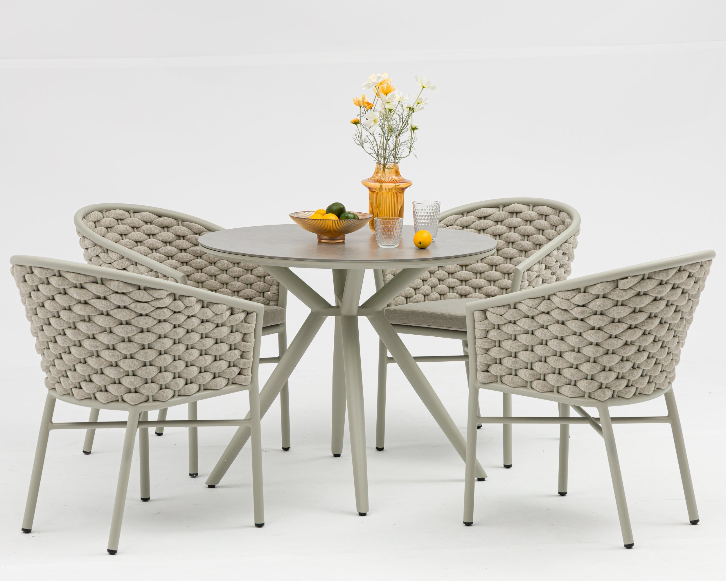 Round outdoor table with four woven chairs on a white background