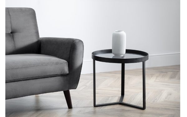 Gray sofa and black side table with a white cylindrical object in a minimalistic room.