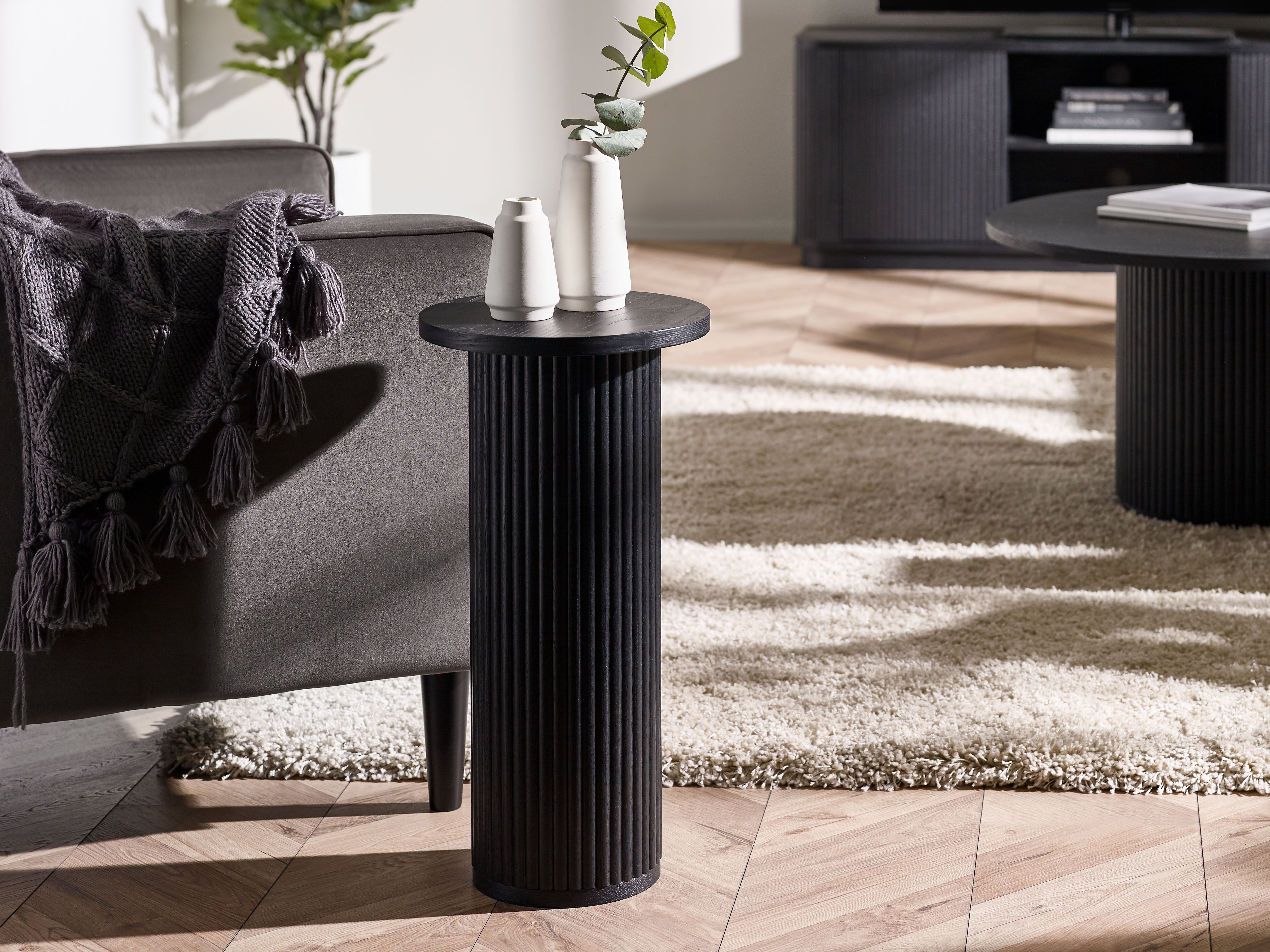 Black side table in a living room setting with a sofa and decorative items.