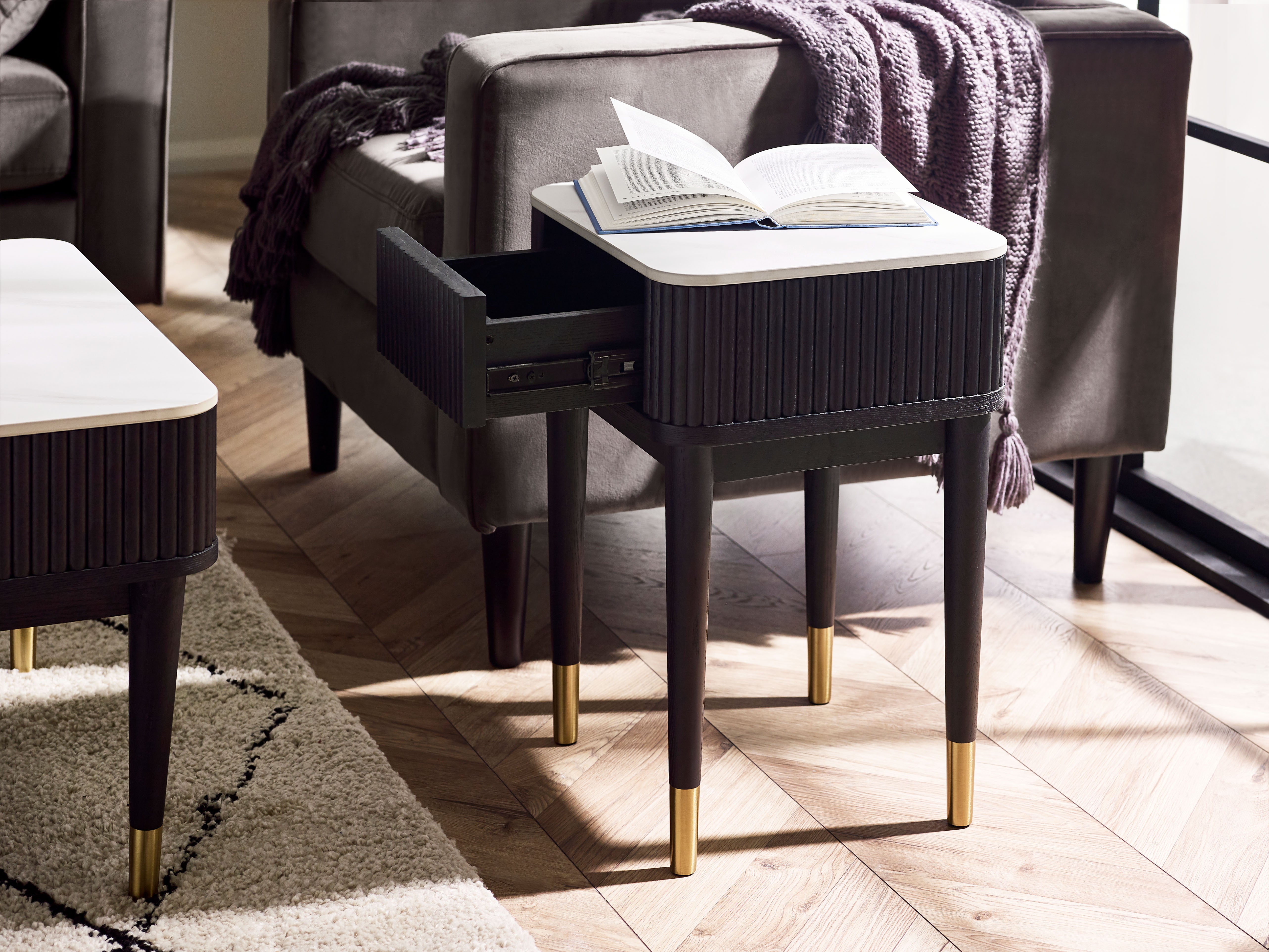 Modern side table with open book on a gray sofa in a living room setting