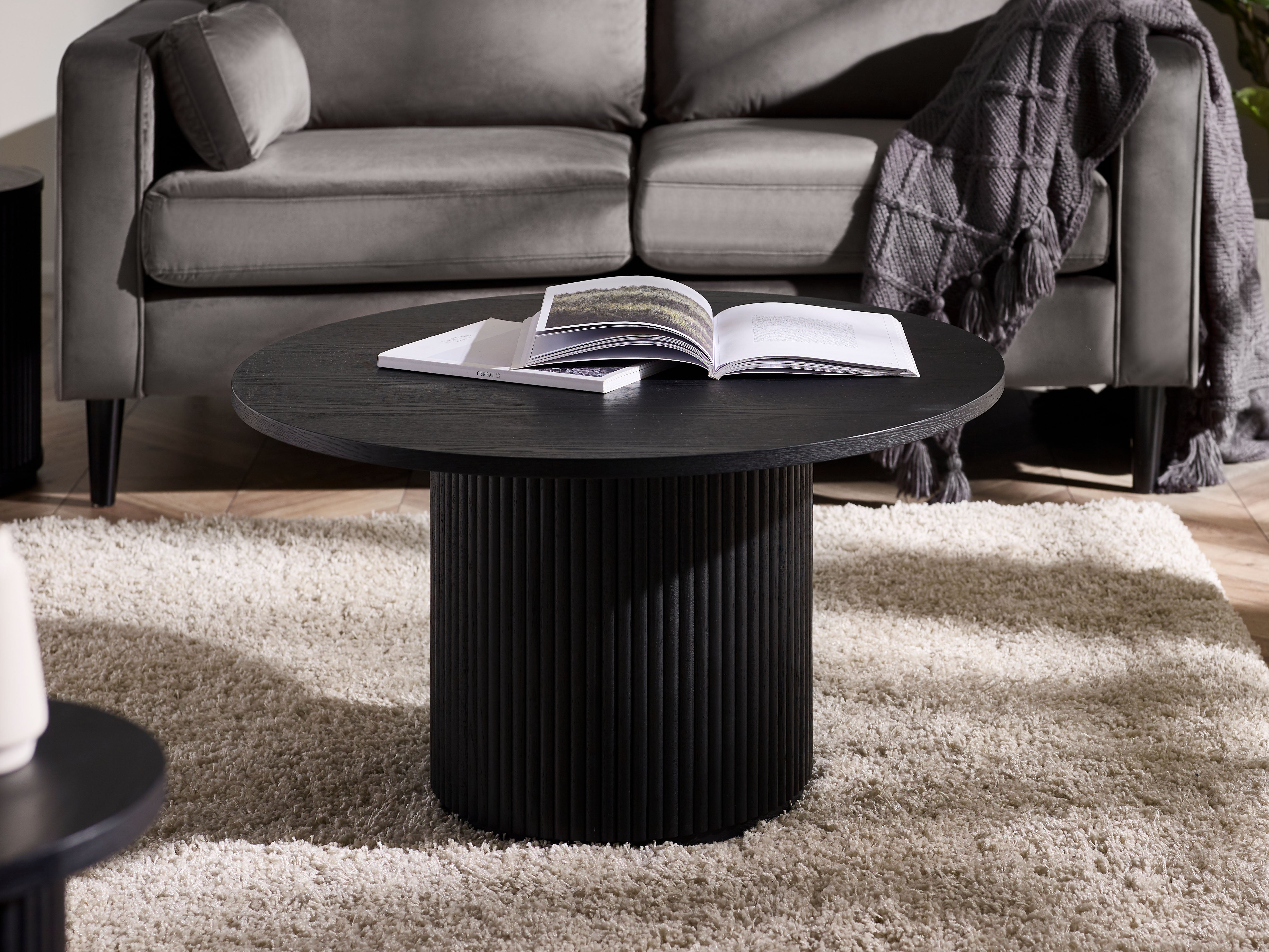 Black coffee table with an open book on a gray sofa in a living room setting.