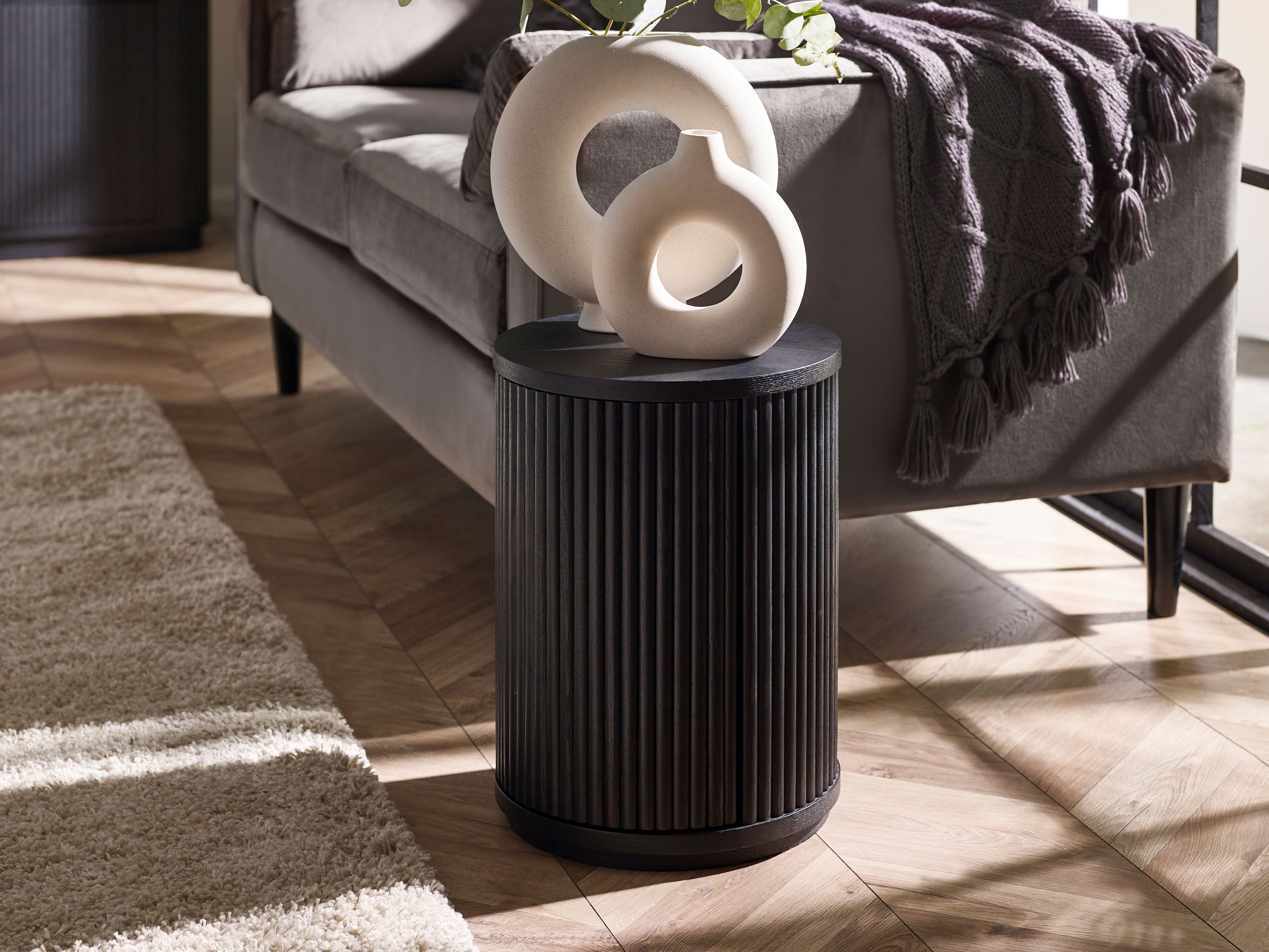 Black cylindrical side table with decorative white sculpture in a living room setting.