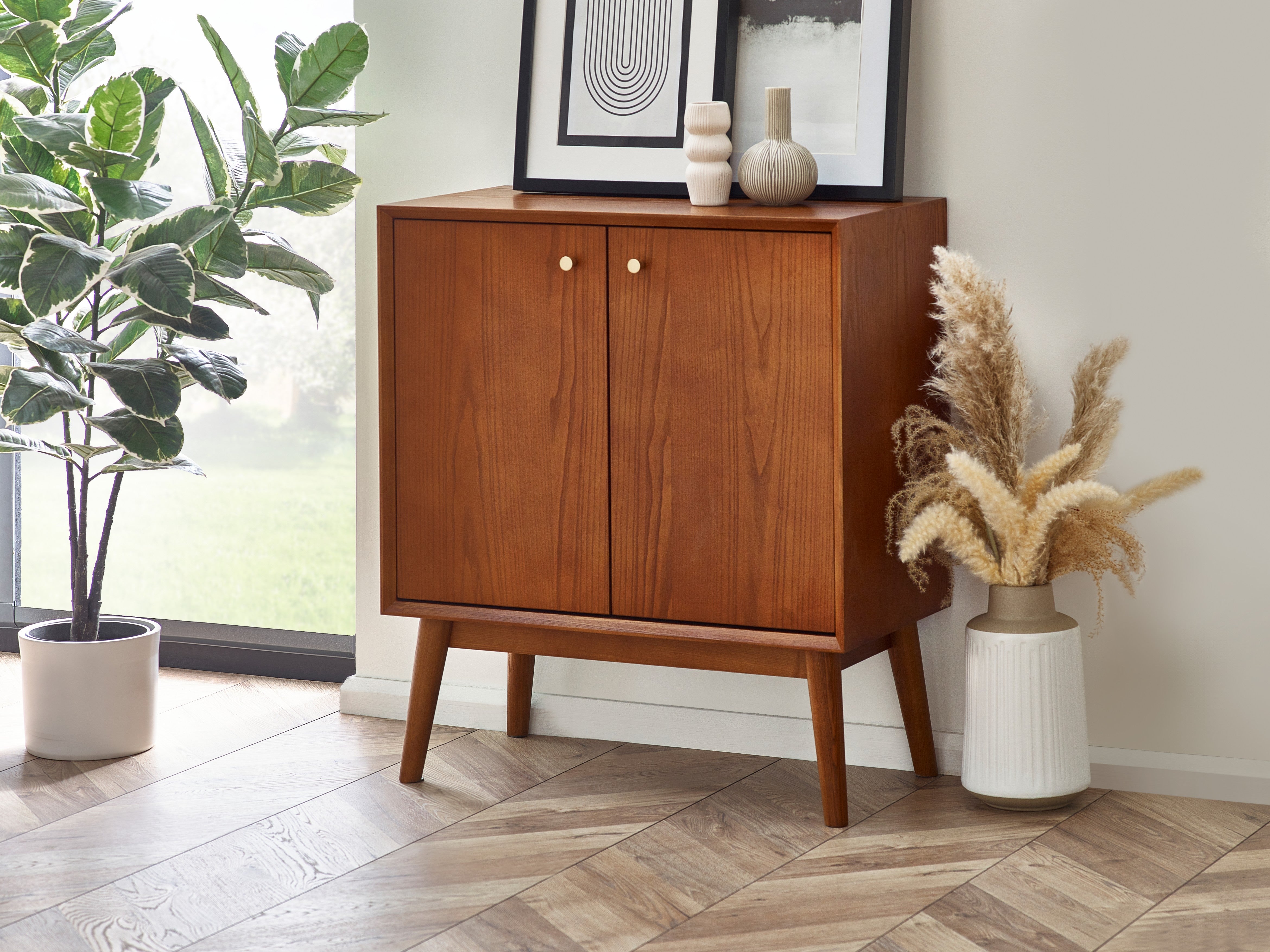 Wooden cabinet with decorative items in a room with plants and a vase.