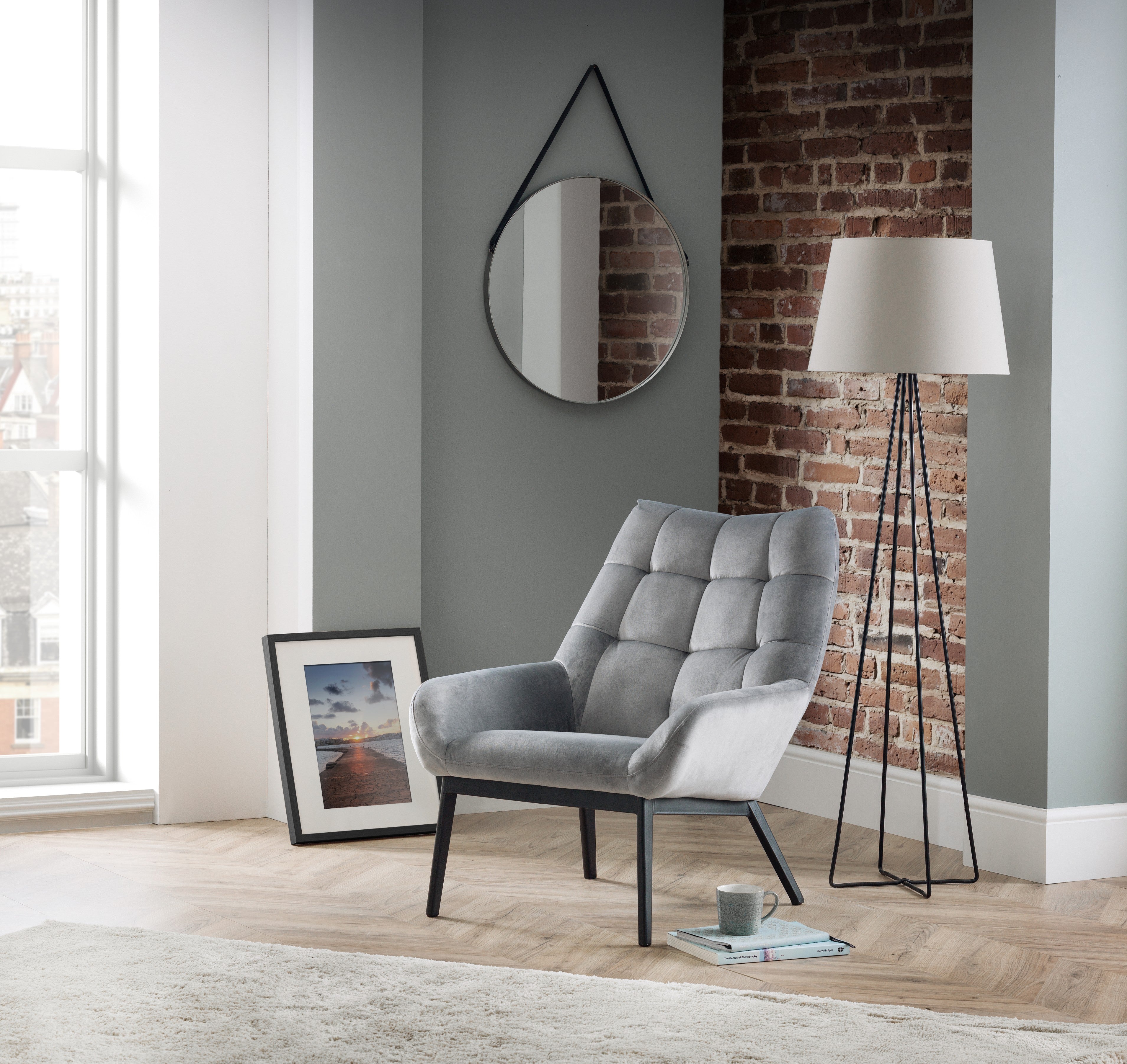 Gray armchair in a modern living room with a brick wall and floor lamp.