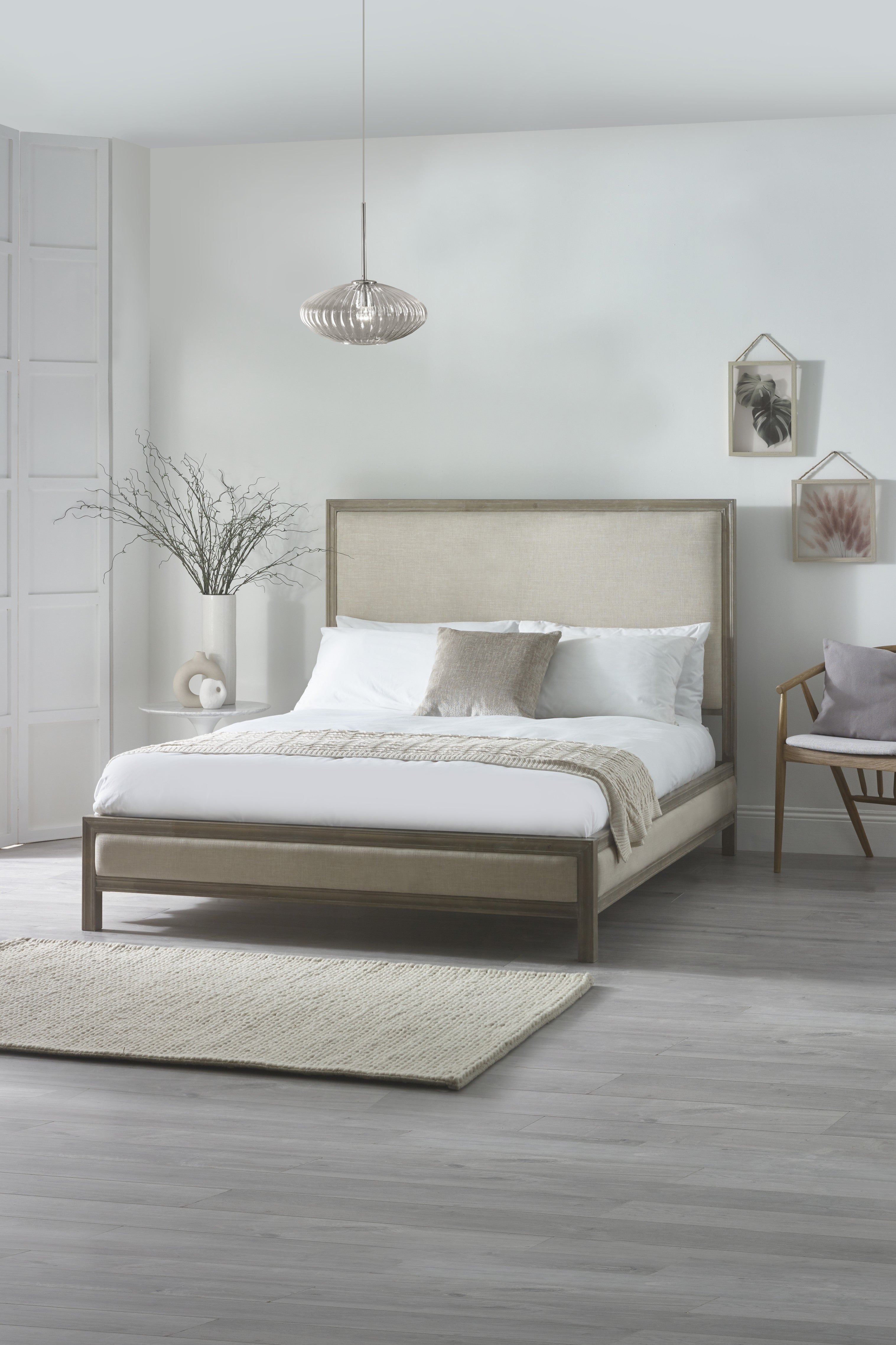 Neatly made bed in a modern bedroom with light wood flooring and decor.