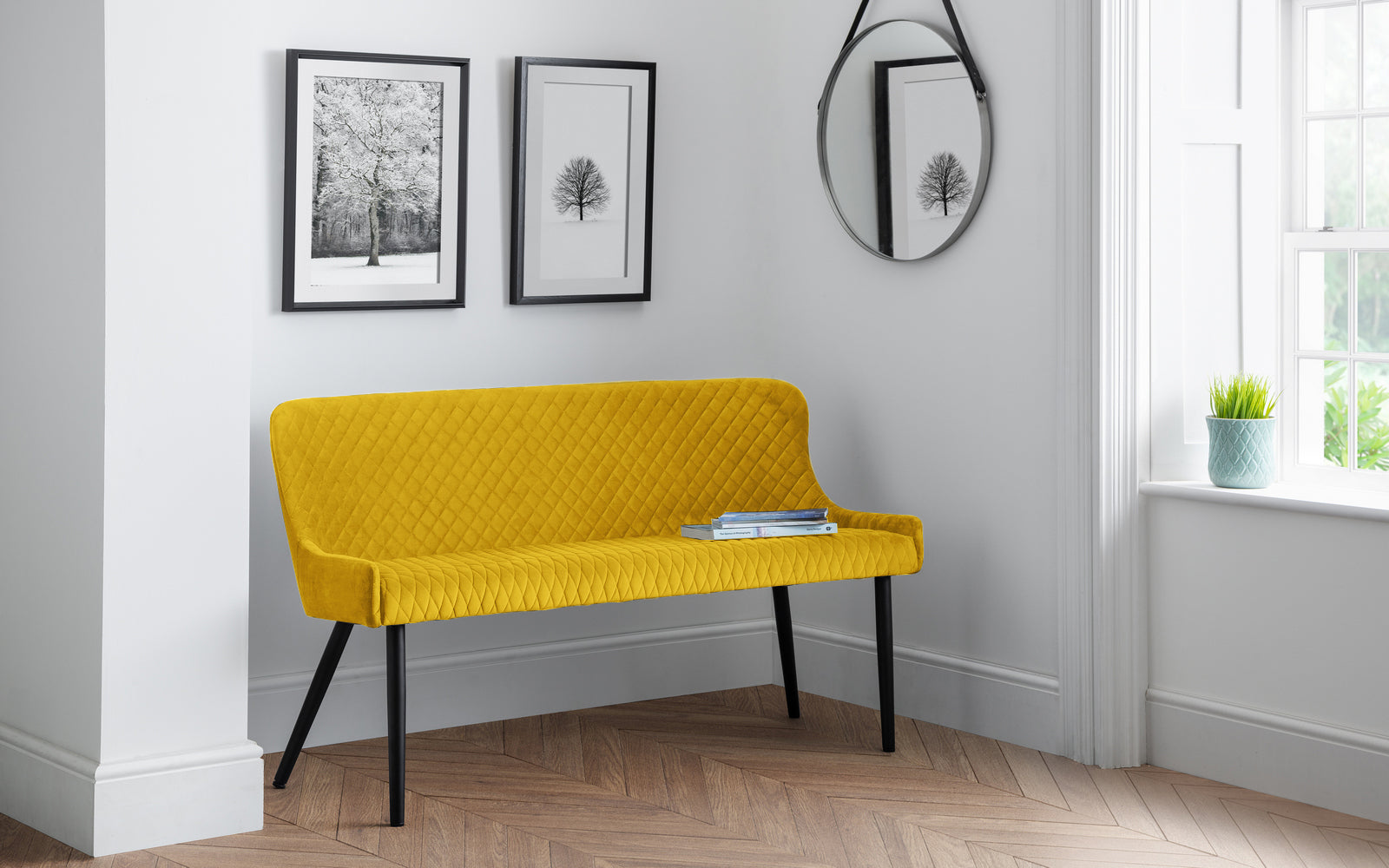 Yellow bench in a room with framed pictures on the wall and a window.