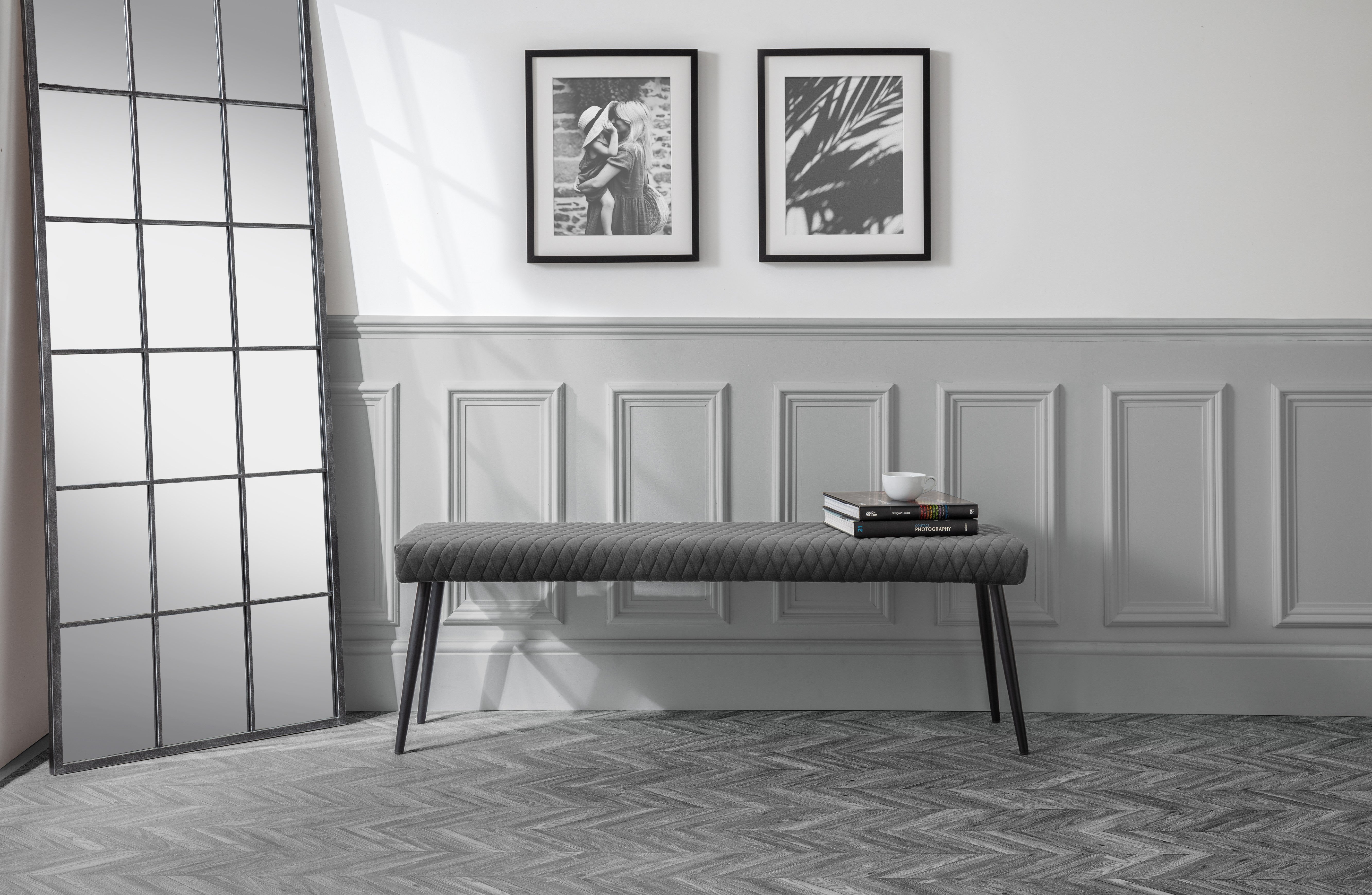 Gray upholstered bench in a room with framed pictures on the wall.