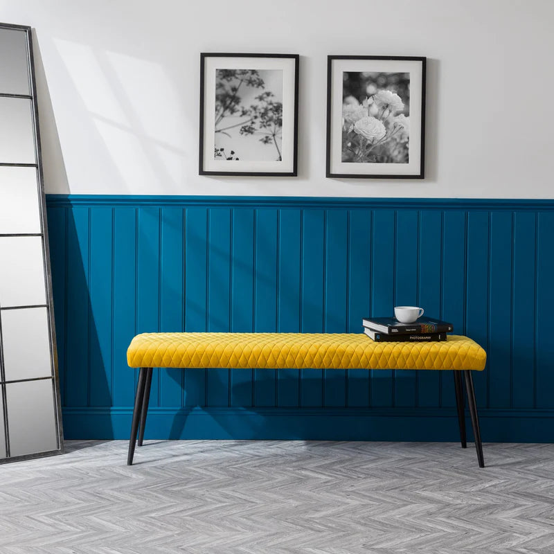 Yellow bench against a blue paneled wall with two framed pictures.