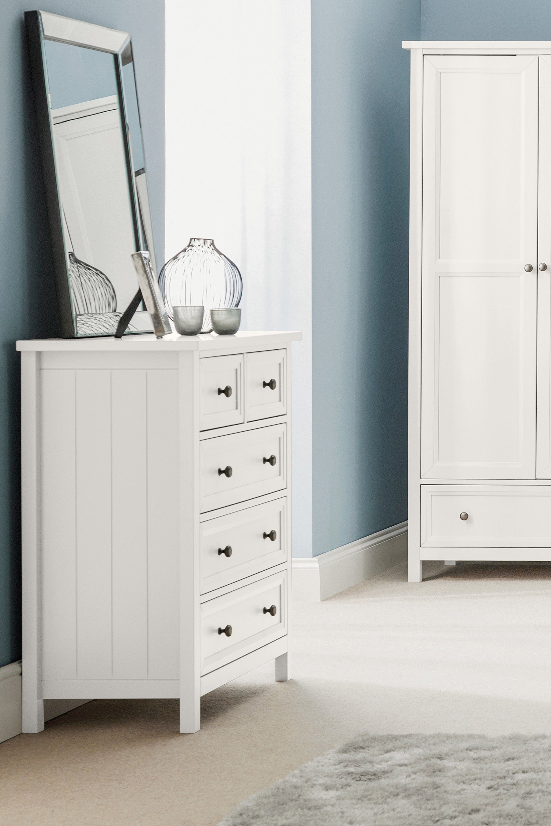 White bedroom furniture set with dresser and wardrobe against a blue wall.