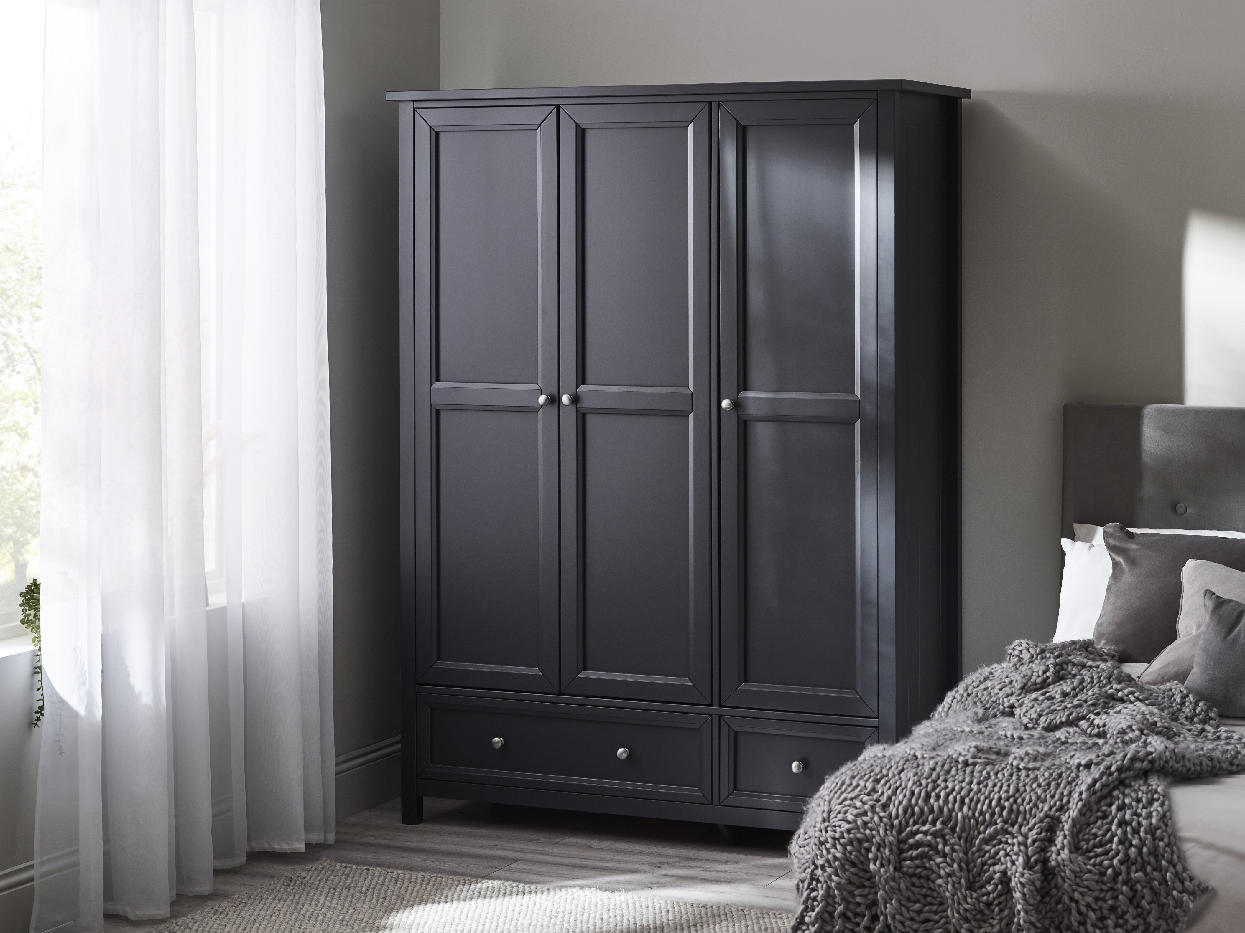 Black wardrobe in a bedroom with a bed and curtains.