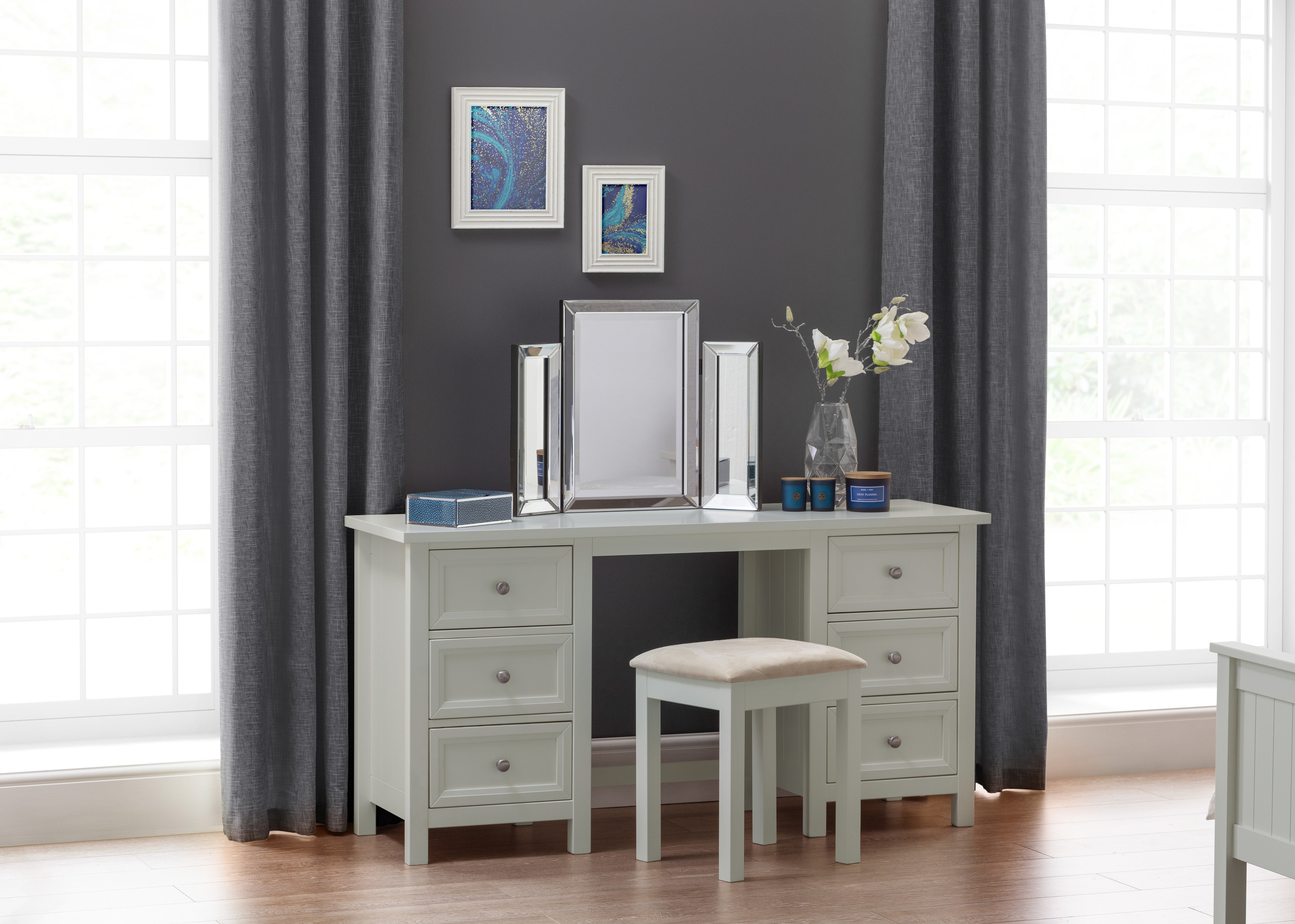 Dressing table with mirror, stool, and decorative items in a room with gray walls and curtains.