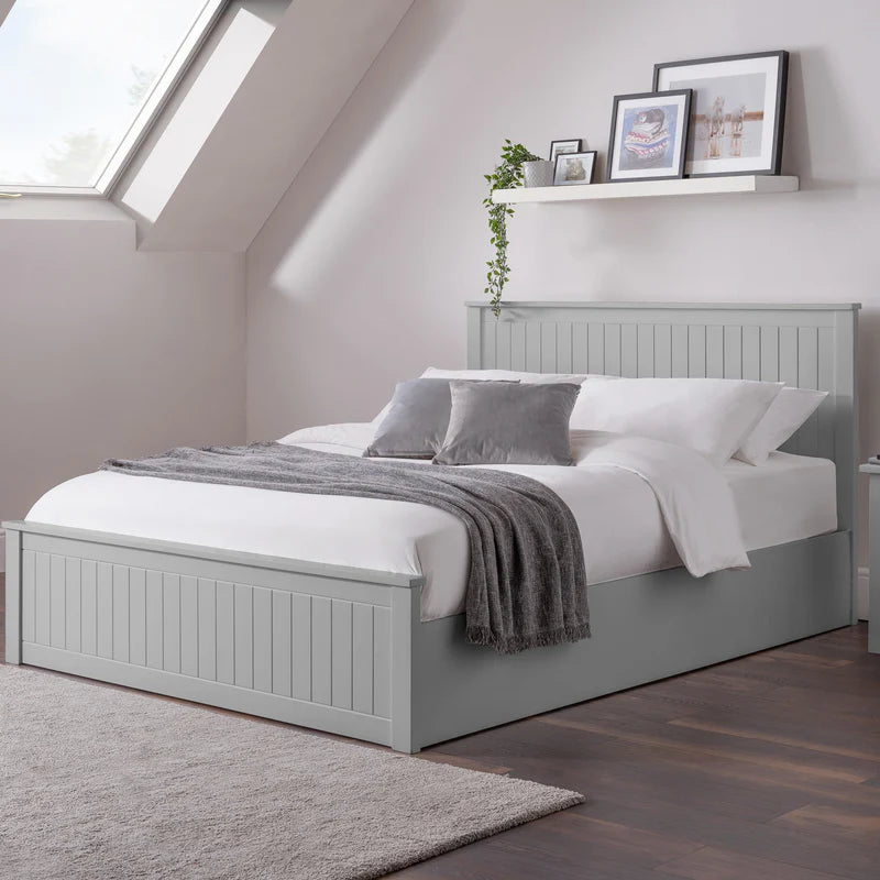 Gray bed in a bedroom with a window and shelves in the background