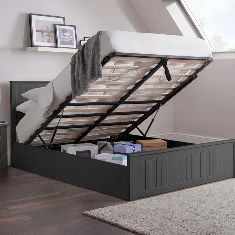 Grey bed with open storage compartment in a room with framed pictures on the wall.