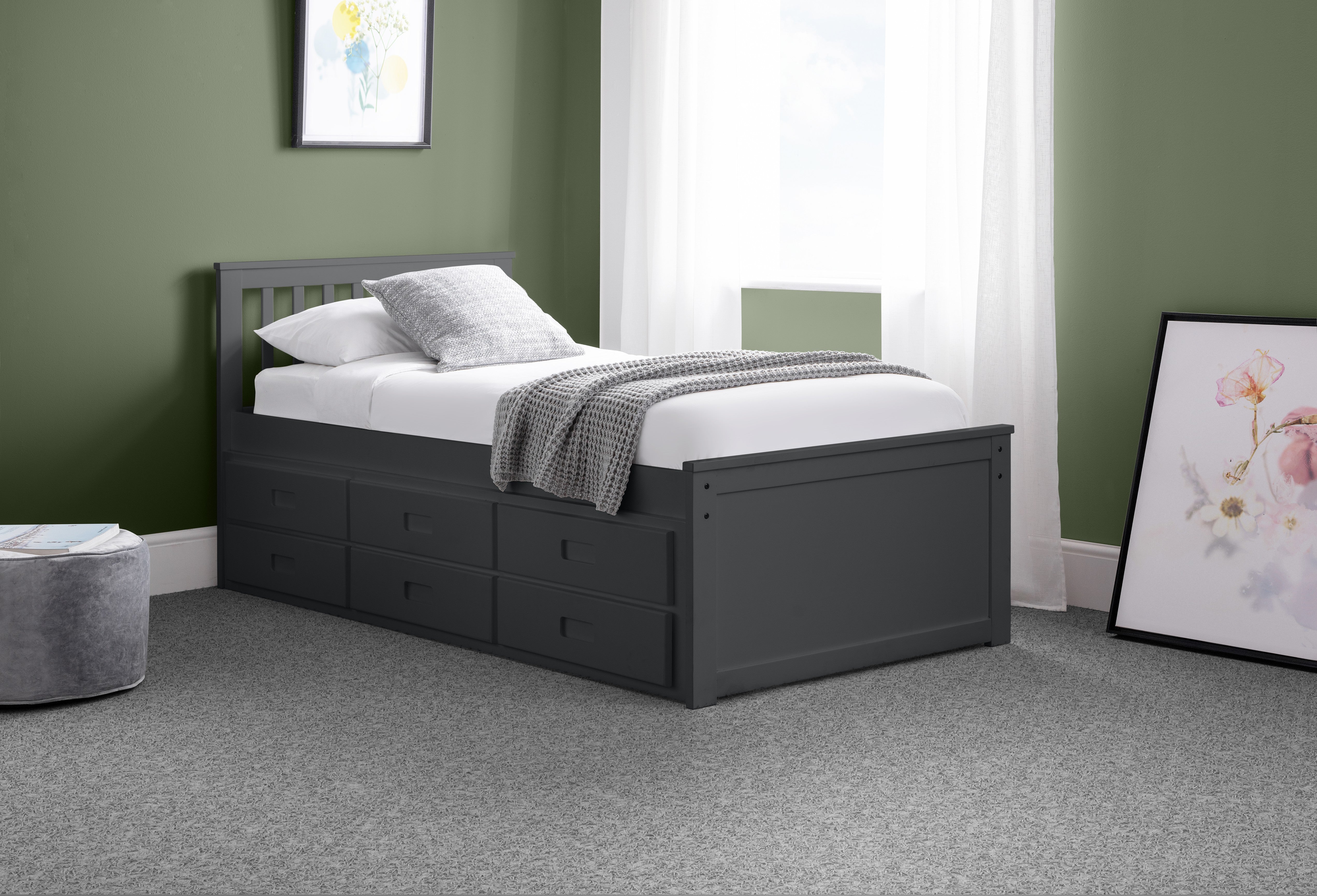 Gray bed with storage drawers in a room with green walls and white curtains.